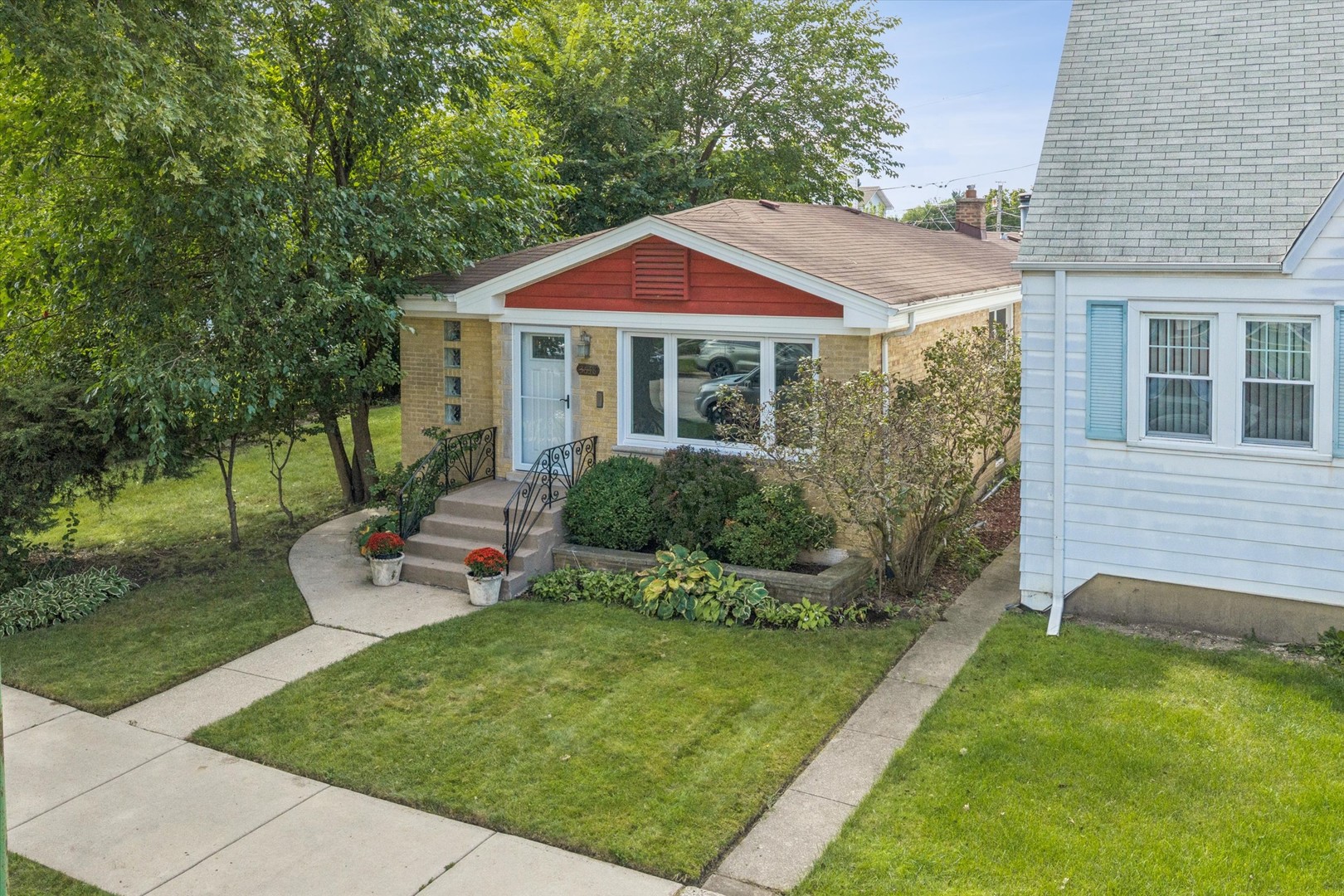 Brick home with red front gable, white entry, landscaped lawn, and mature trees.