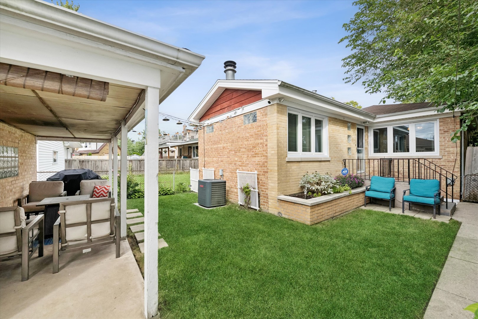 Brick home’s backyard with a covered dining patio, sunroom, lawn, and paved seating area.