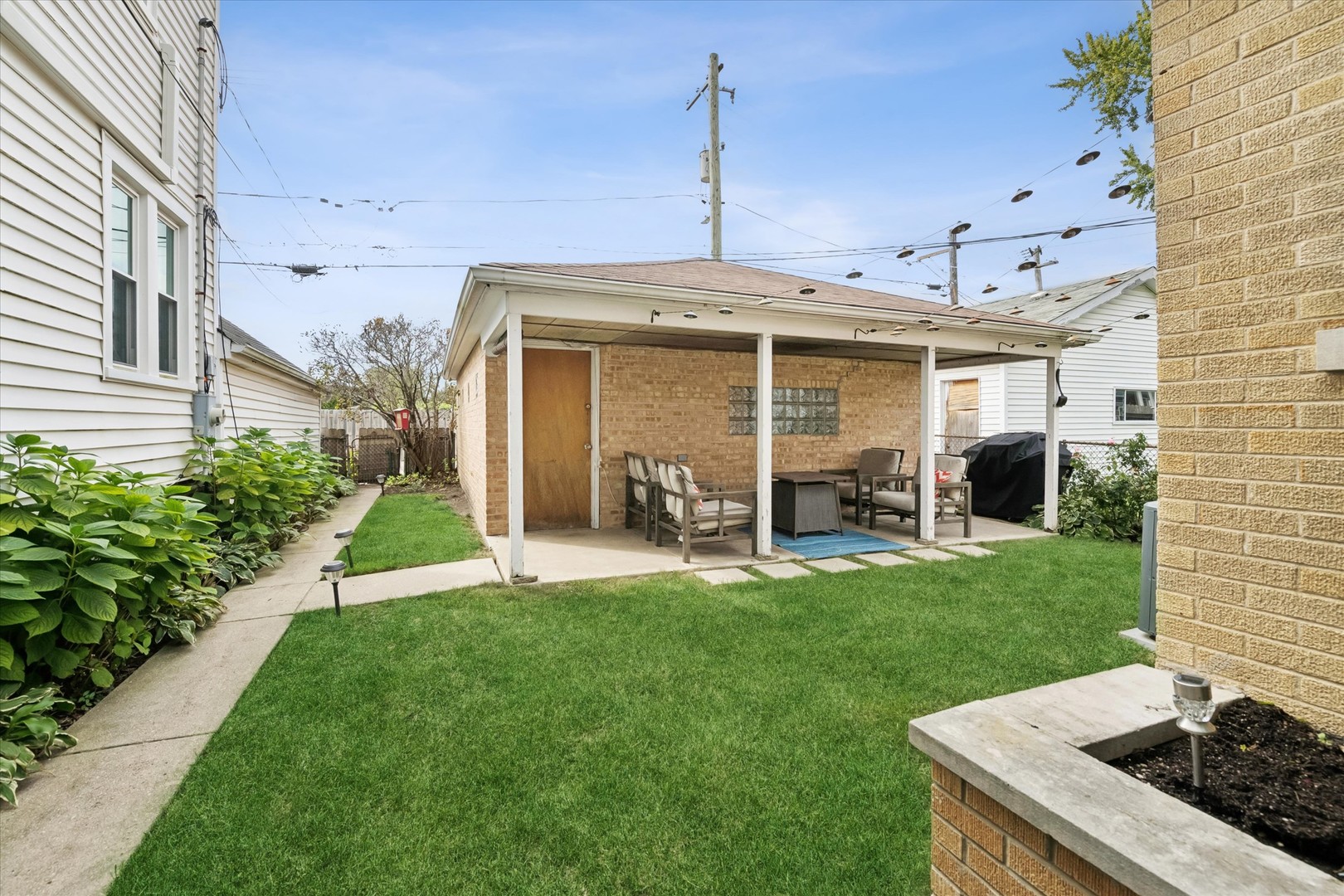 Backyard lawn and covered brick patio with outdoor seating and dining table.