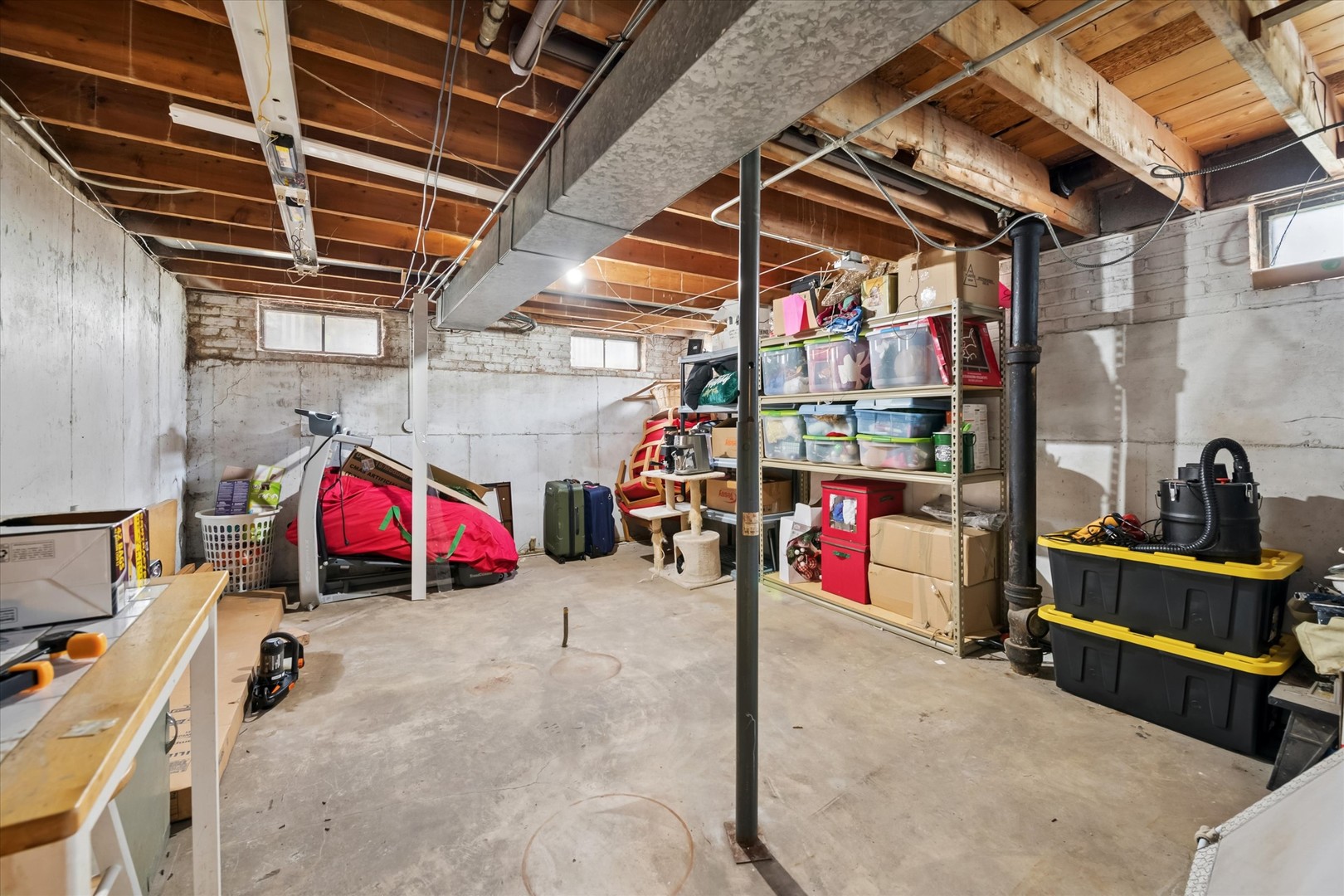 Unfinished basement with exposed joists, storage shelves, a treadmill, and concrete floor.