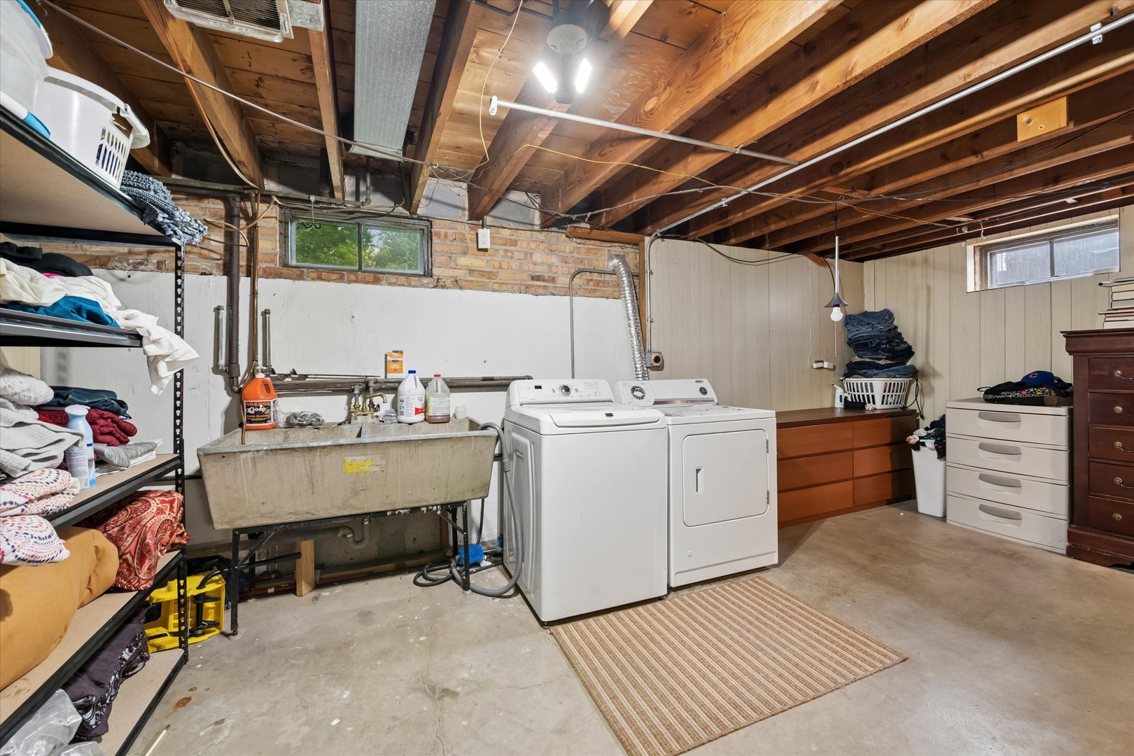 Basement laundry area with washer and dryer, utility sink, and exposed ceiling joists.