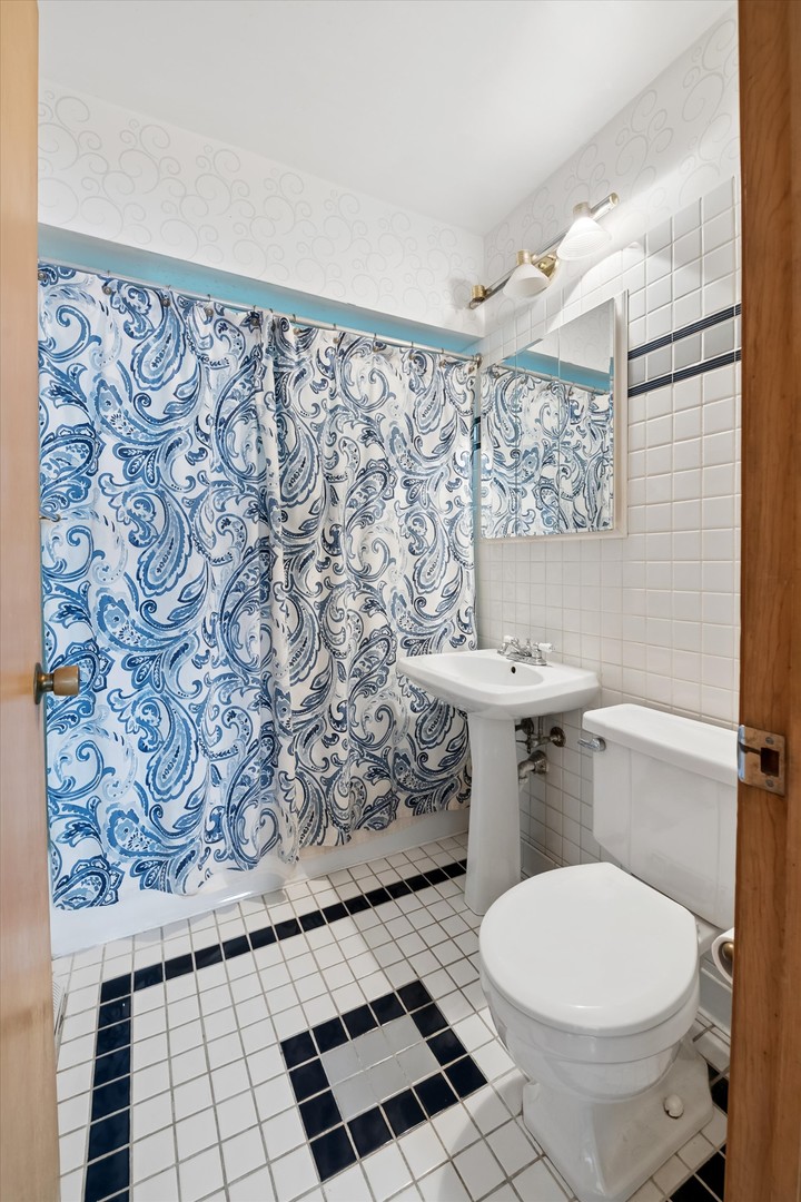 Bathroom with a blue-and-white paisley shower curtain and dark floor tile accents.