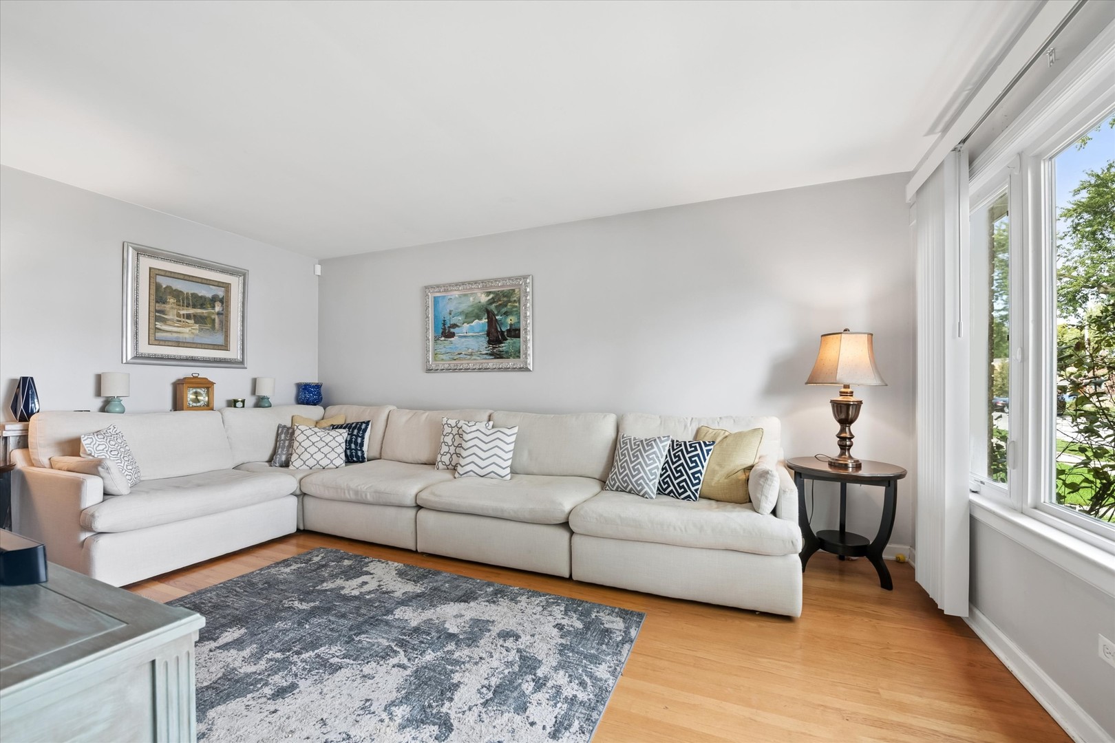Living room with a white sectional, patterned rug, hardwood floors, and tall windows.