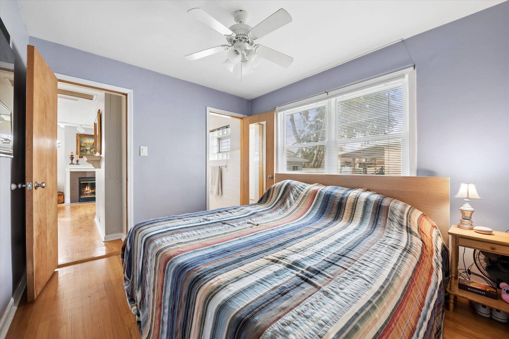 Bedroom with a striped quilt, ceiling fan, and large window overlooking the street.