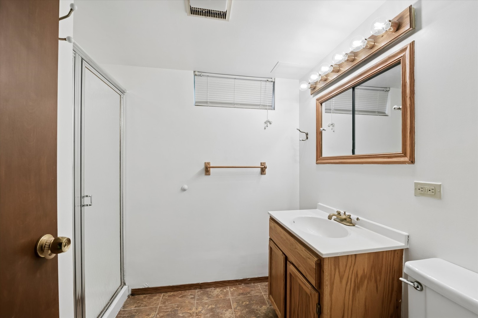 Bathroom with a glass shower, wood vanity, framed mirror, and brown tile floor.