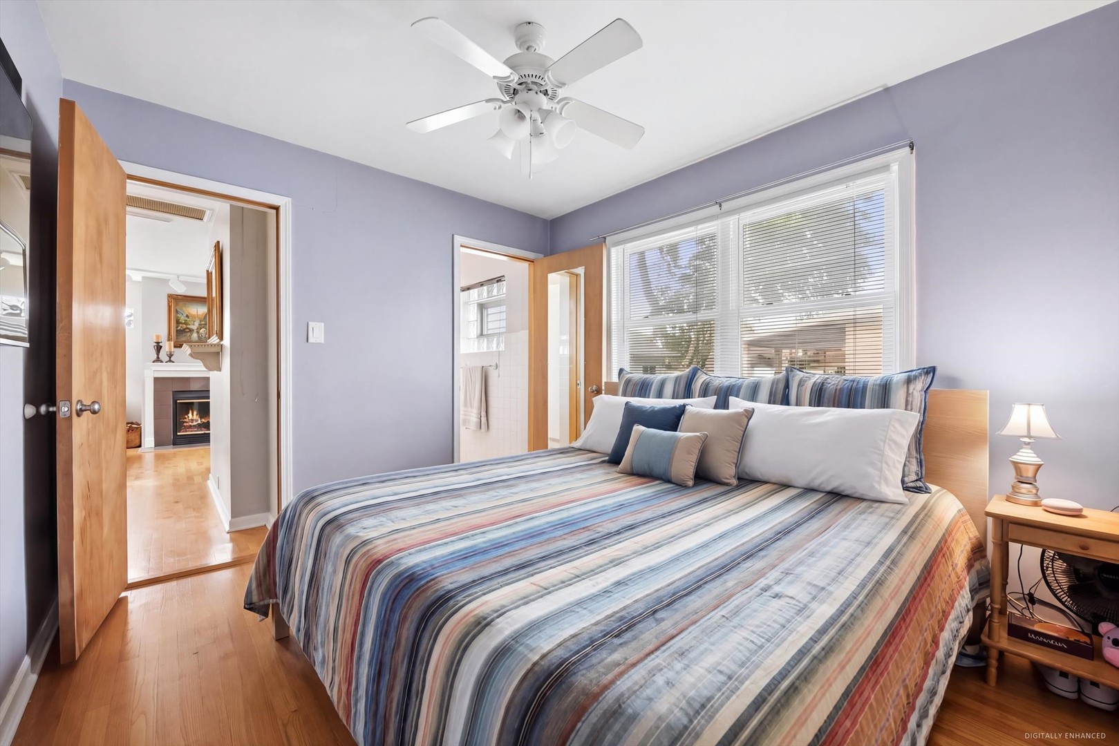 Bedroom with a striped bedspread, lavender walls, and windows overlooking the yard.