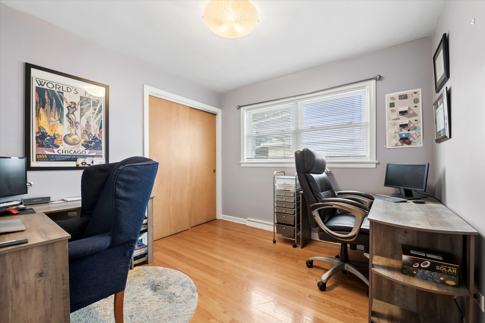 Home office with two workstations, wood floors, and a Chicago World's Fair poster.