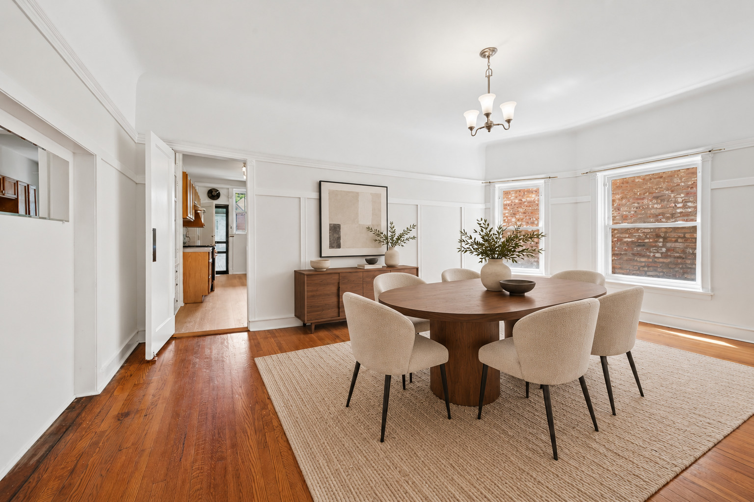 Dining room with an oval wood table, upholstered chairs, hardwood floors, and white paneled walls.