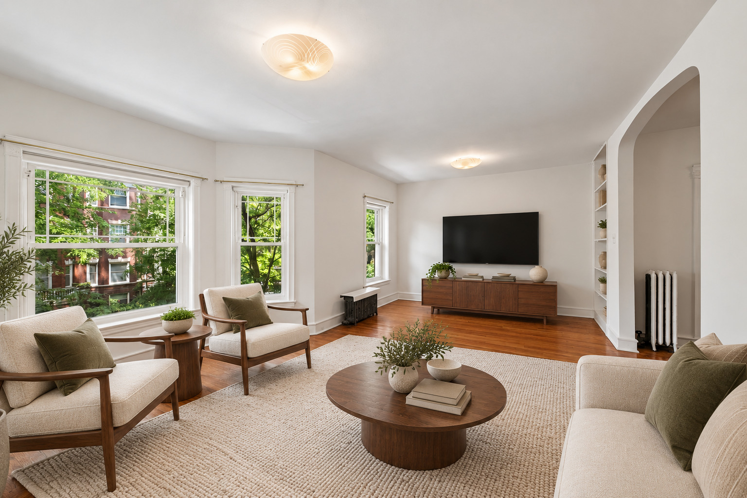 Staged living room with large leafy outlook windows, hardwood floors, and cream seating.