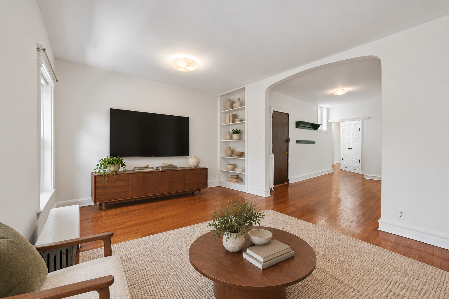 Staged living room with a wood media console, built-in shelves, hardwood floors, and an arched entry opening.