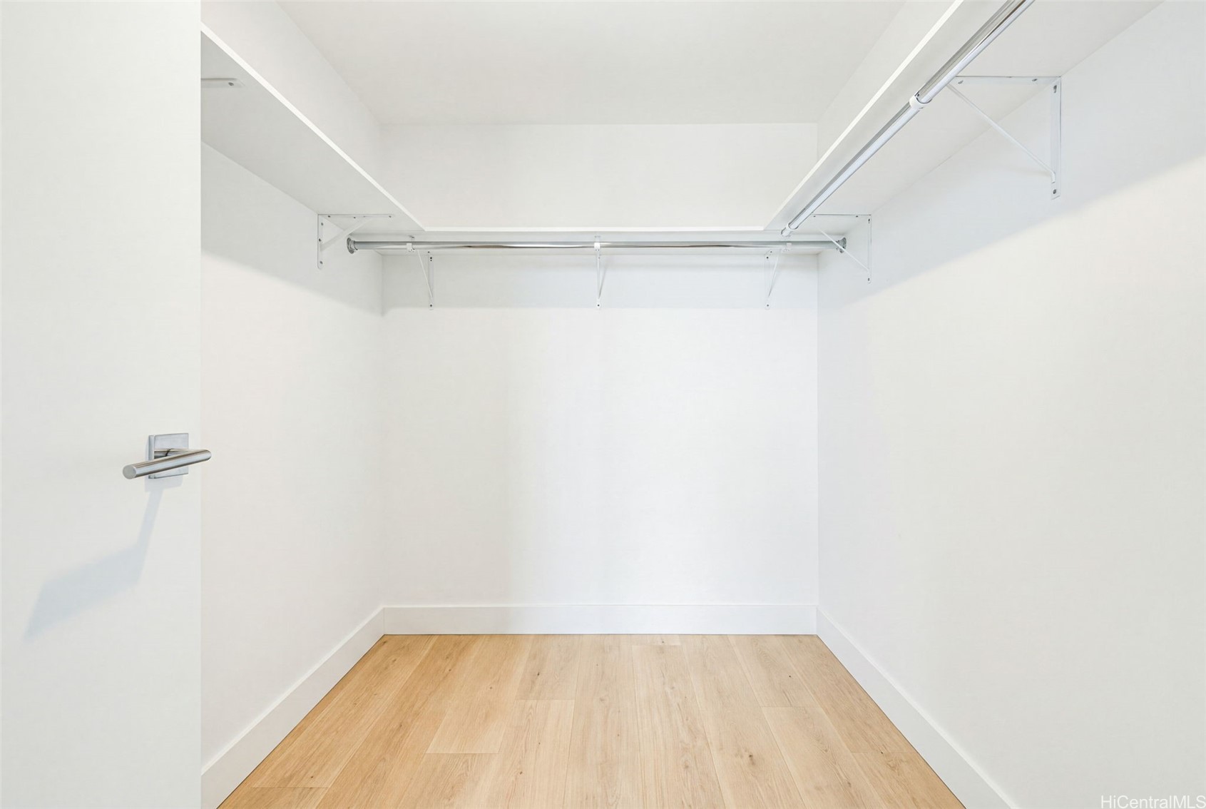 Empty walk-in closet with light wood flooring and overhead metal hanging rods.