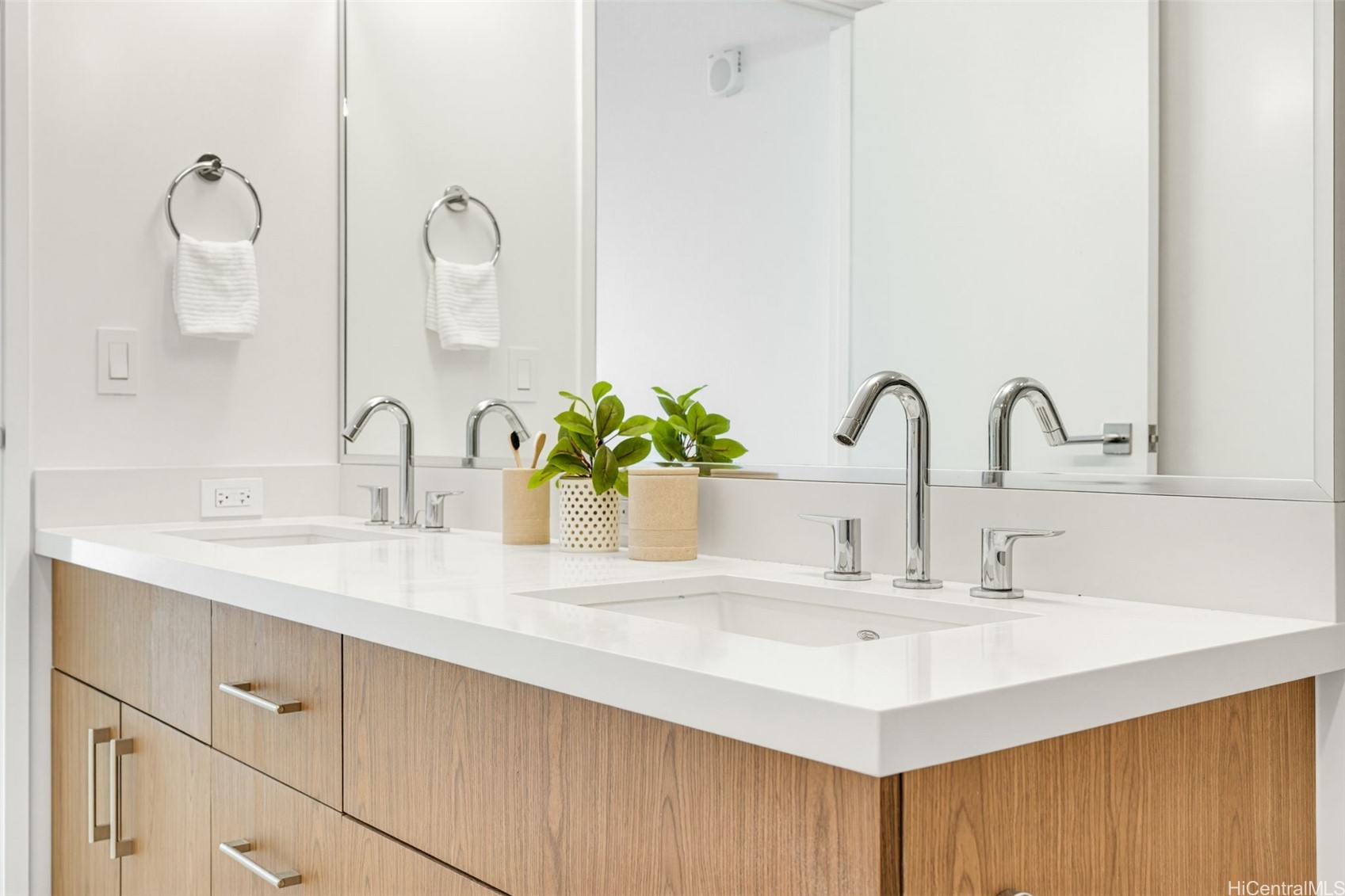 Bathroom vanity with two sinks, chrome faucets, mirrored walls, and light wood cabinetry.