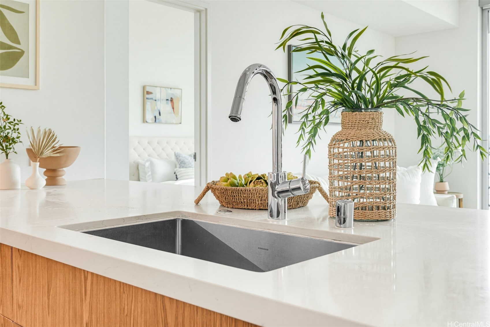 Kitchen sink with a tall chrome faucet, white countertop, and wood-front cabinetry.
