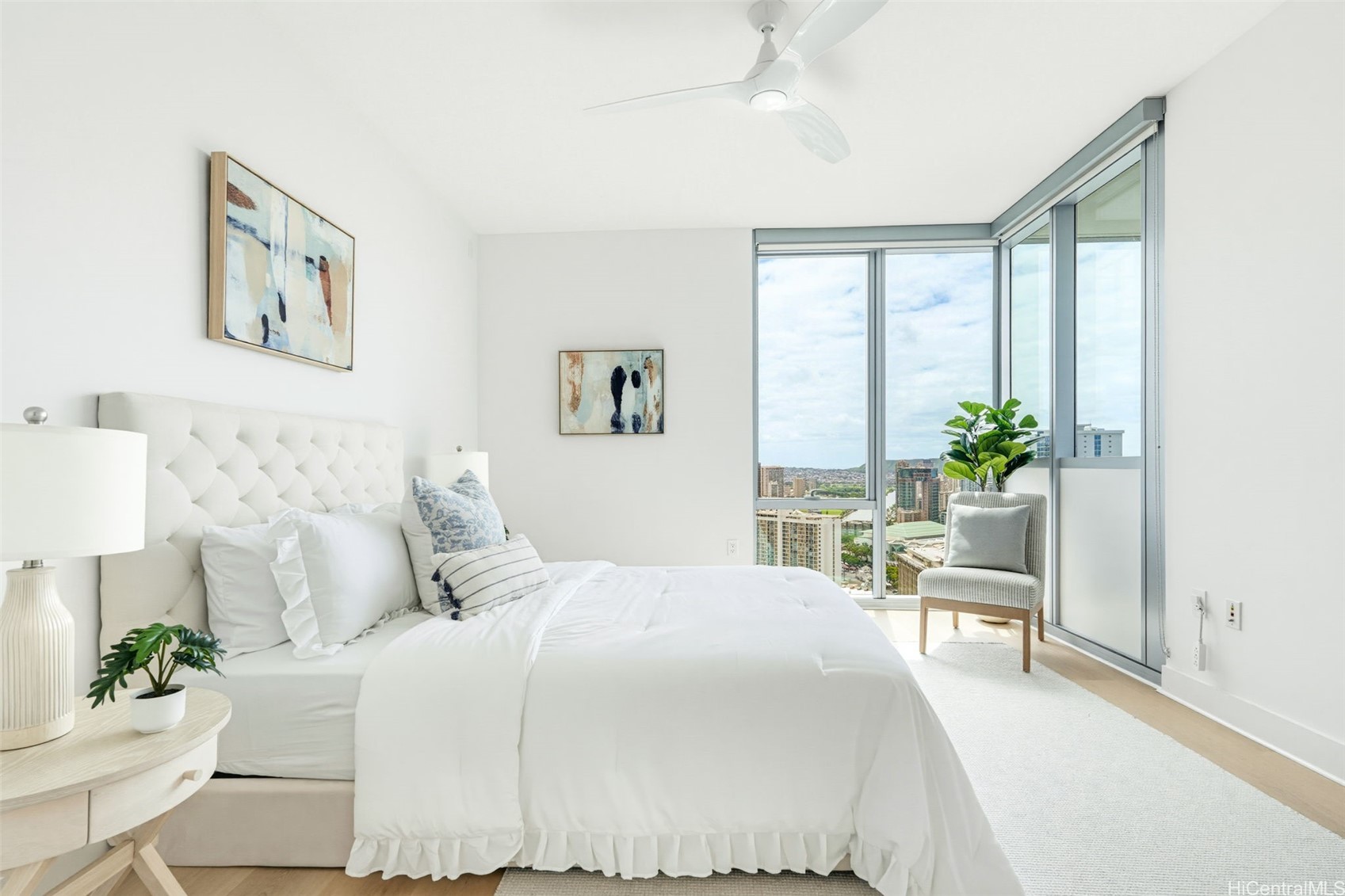 Bright bedroom with white tufted bed and corner windows overlooking Honolulu.