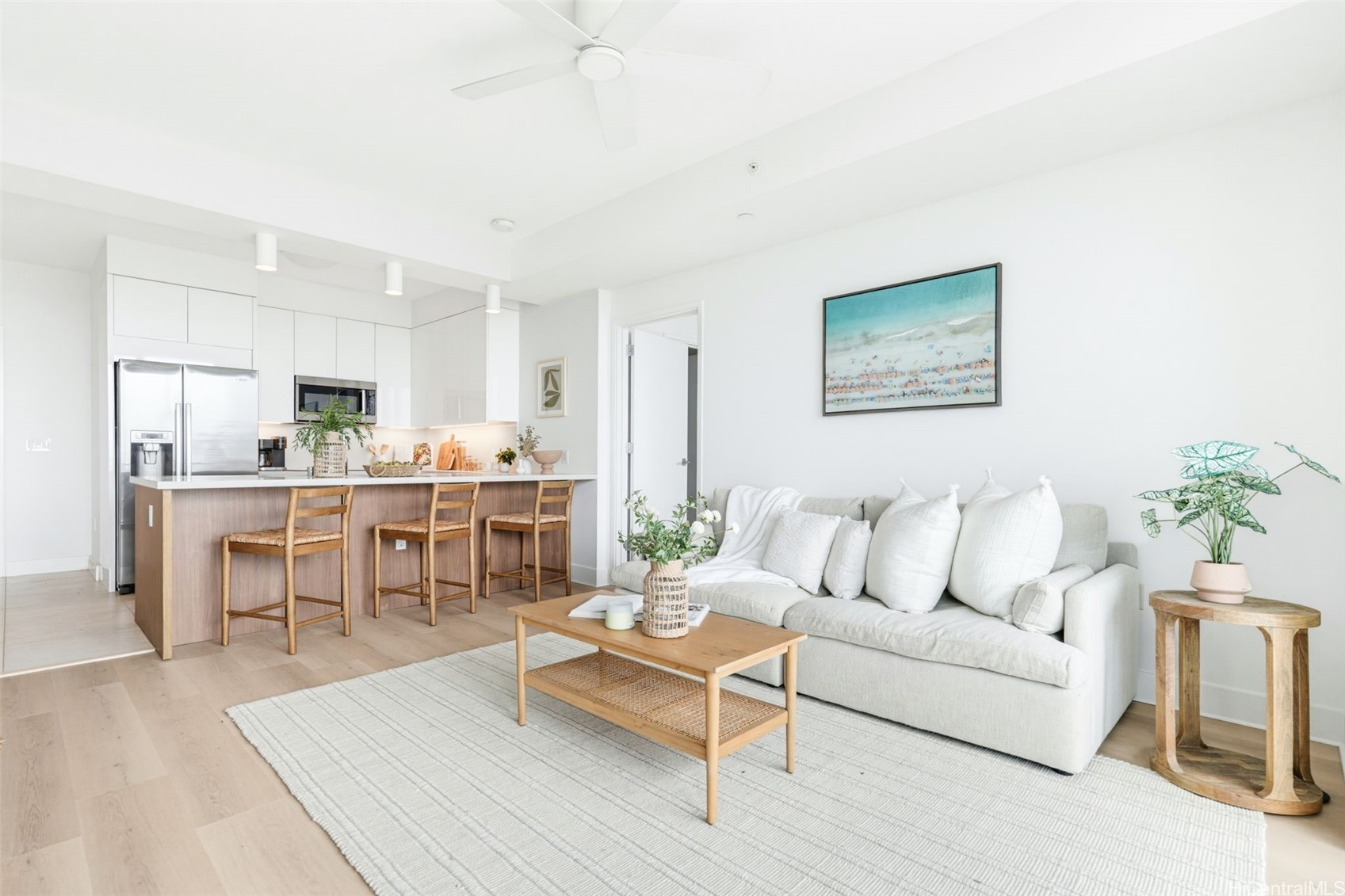 Open-plan living room and kitchen with a wood-front island, white sofa, and pale wood floors.