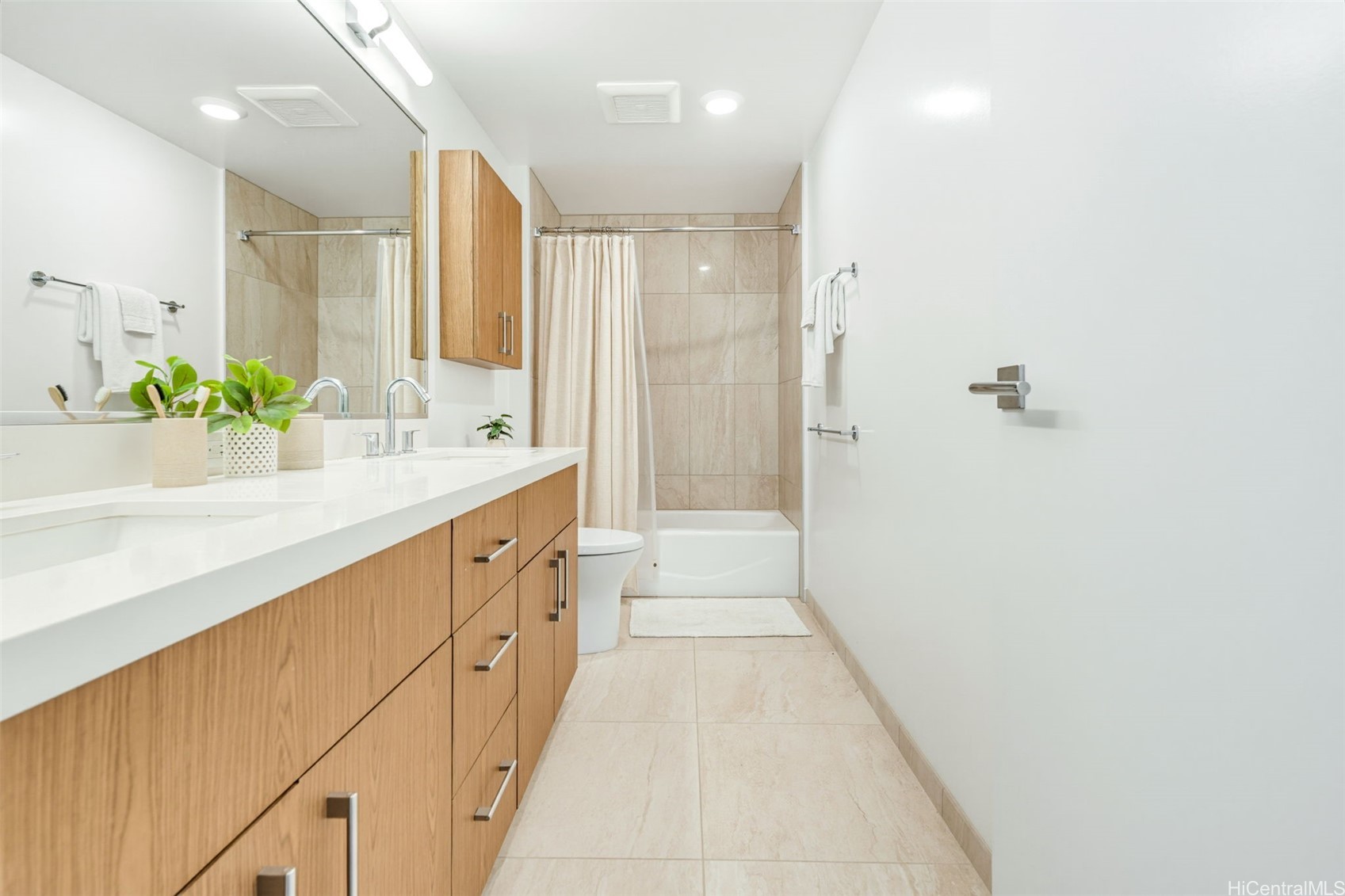 Bathroom with a long wood vanity, large mirror, and beige-tiled tub and shower.
