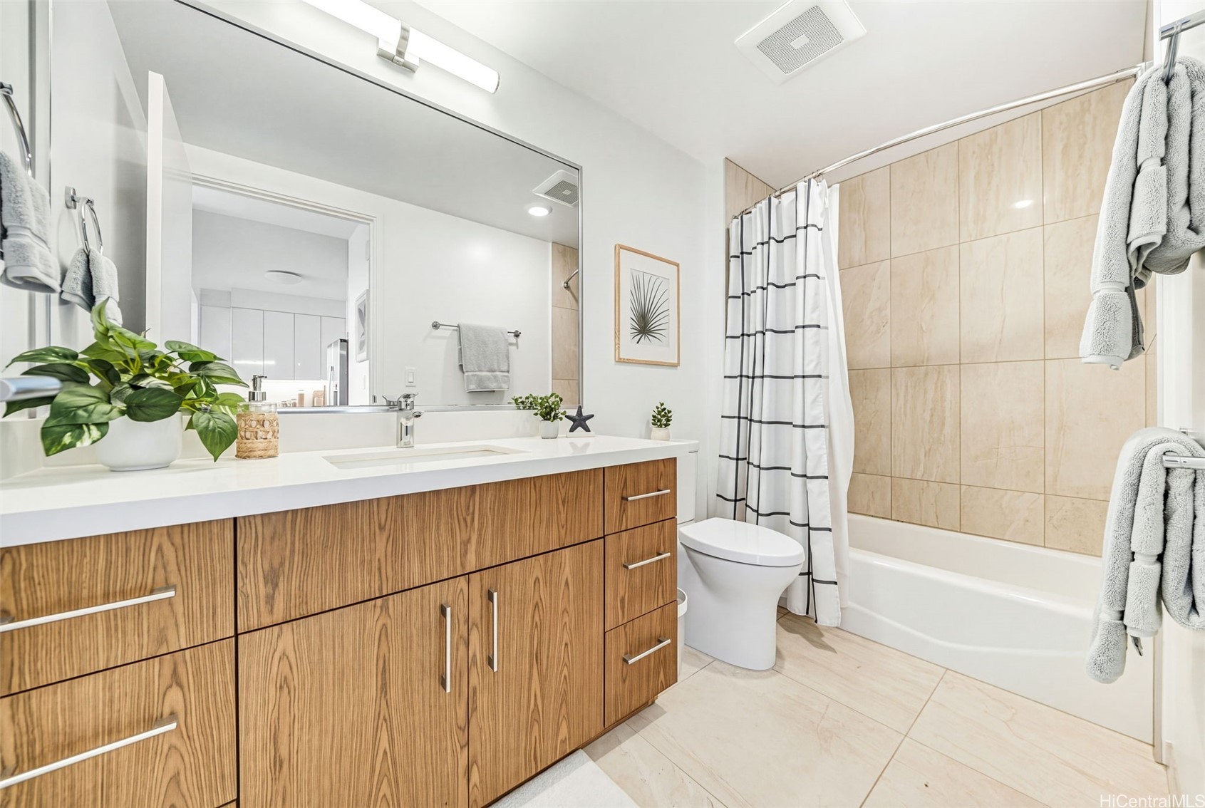Bathroom with a wood-grain vanity, large mirror, and tiled tub-shower.