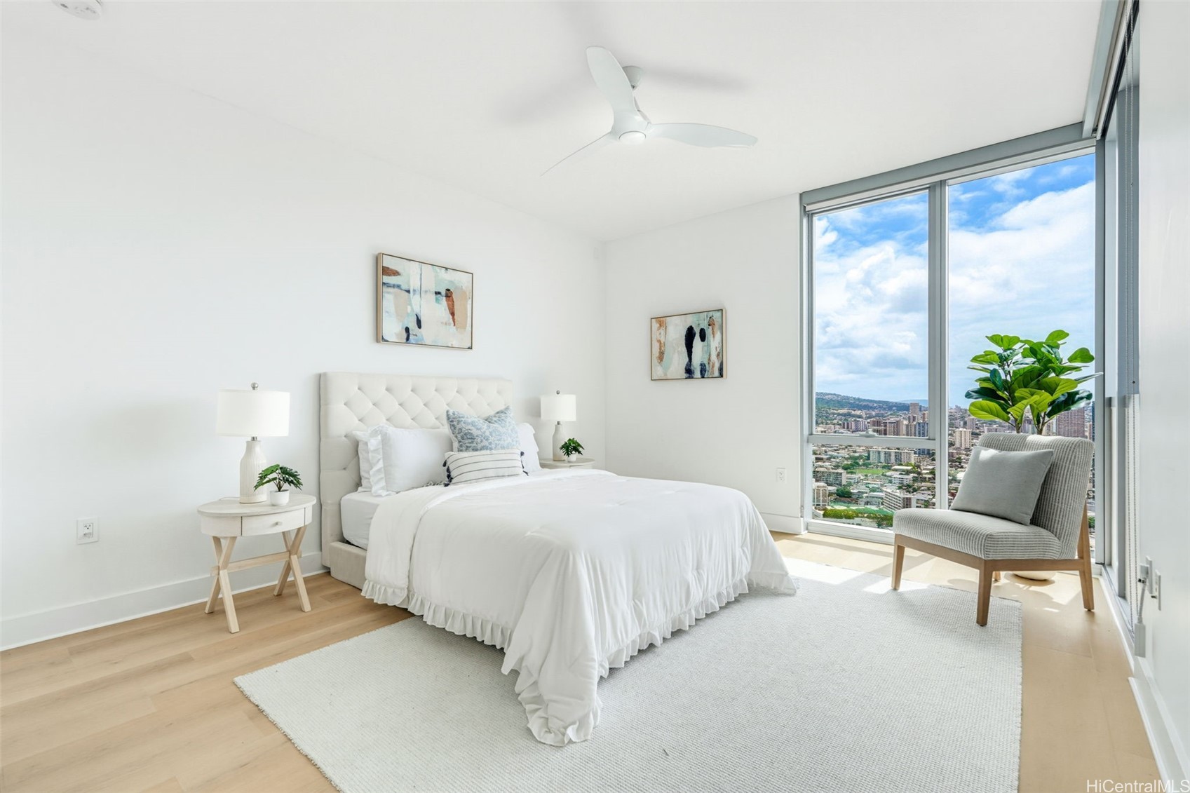 Staged bedroom with a white tufted bed and floor-to-ceiling windows overlooking Honolulu.