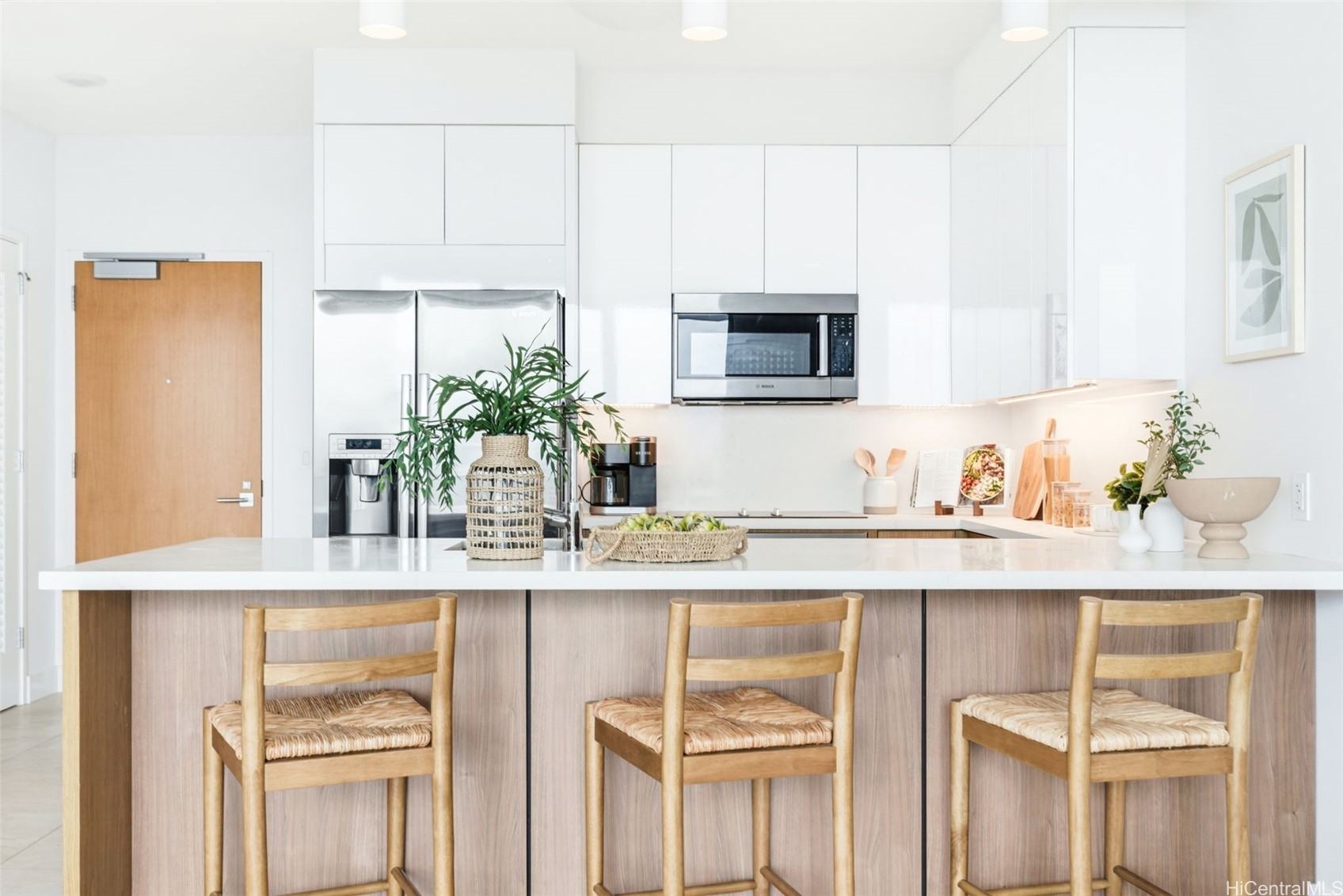 Modern white kitchen with stainless appliances and a wide island lined with three wooden stools.