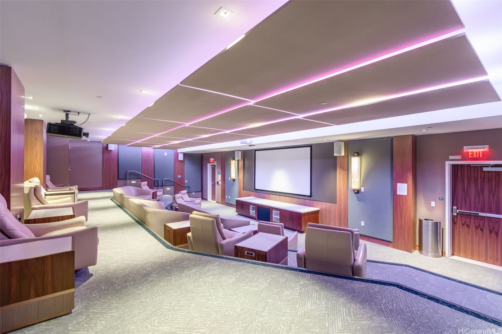 Furnished screening room with upholstered seats, a large projection screen, and pink ceiling lighting.
