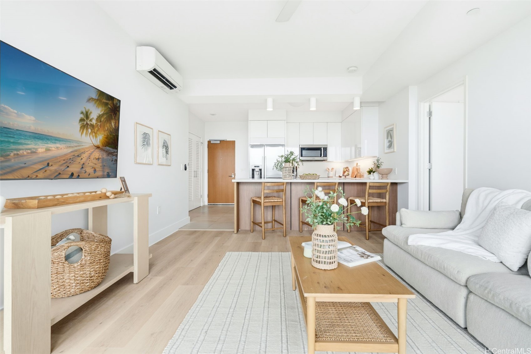 Open-plan living room with a white sectional, wood coffee table, and kitchen breakfast bar.