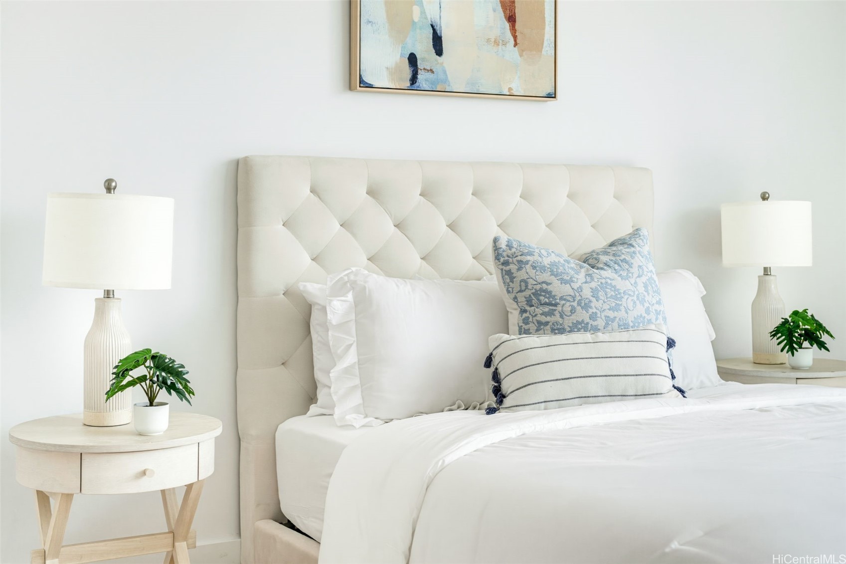 Bedroom with a cream tufted headboard, blue accent pillows, and matching bedside tables and lamps.