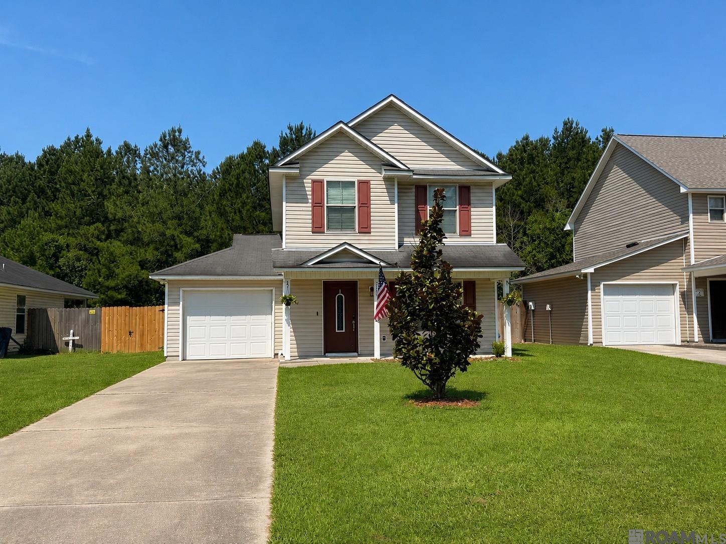 Two-story beige house with red shutters, an attached garage, and a flag by the front door.