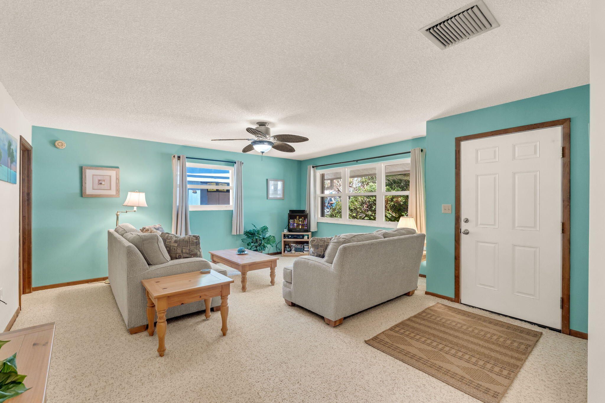 Furnished living room with turquoise walls, beige seating, wooden tables, and a ceiling fan.