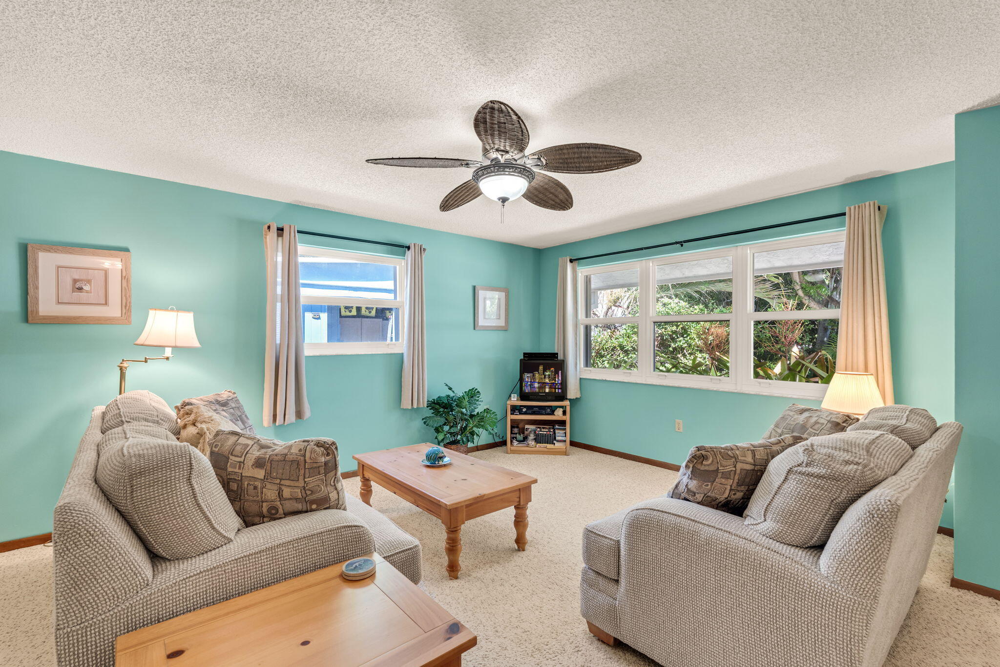 Living room with turquoise walls, two sofas, a wooden coffee table, and wide windows overlooking greenery.