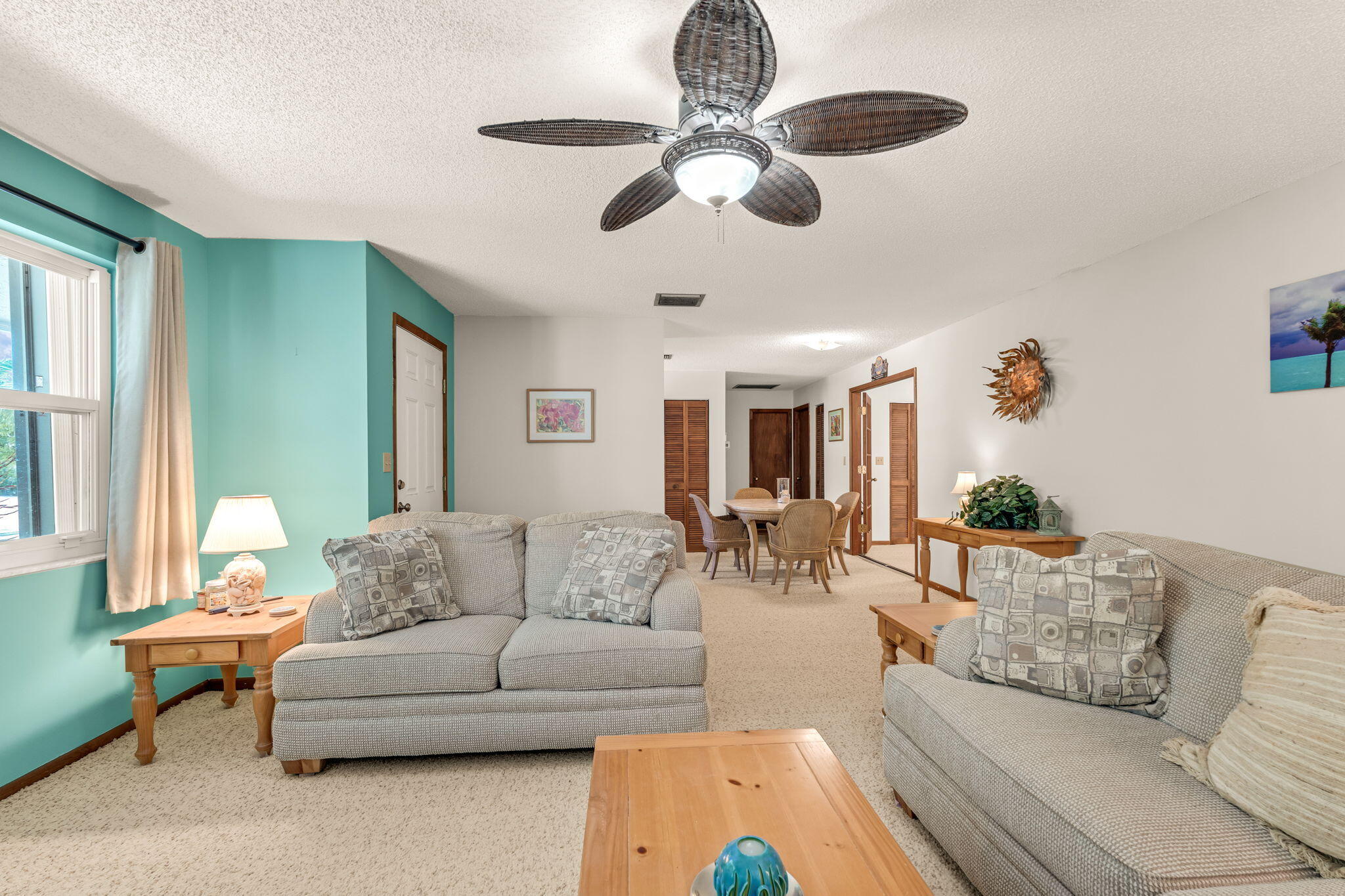 Living room with gray sofas and turquoise accent wall, opening to a dining area.