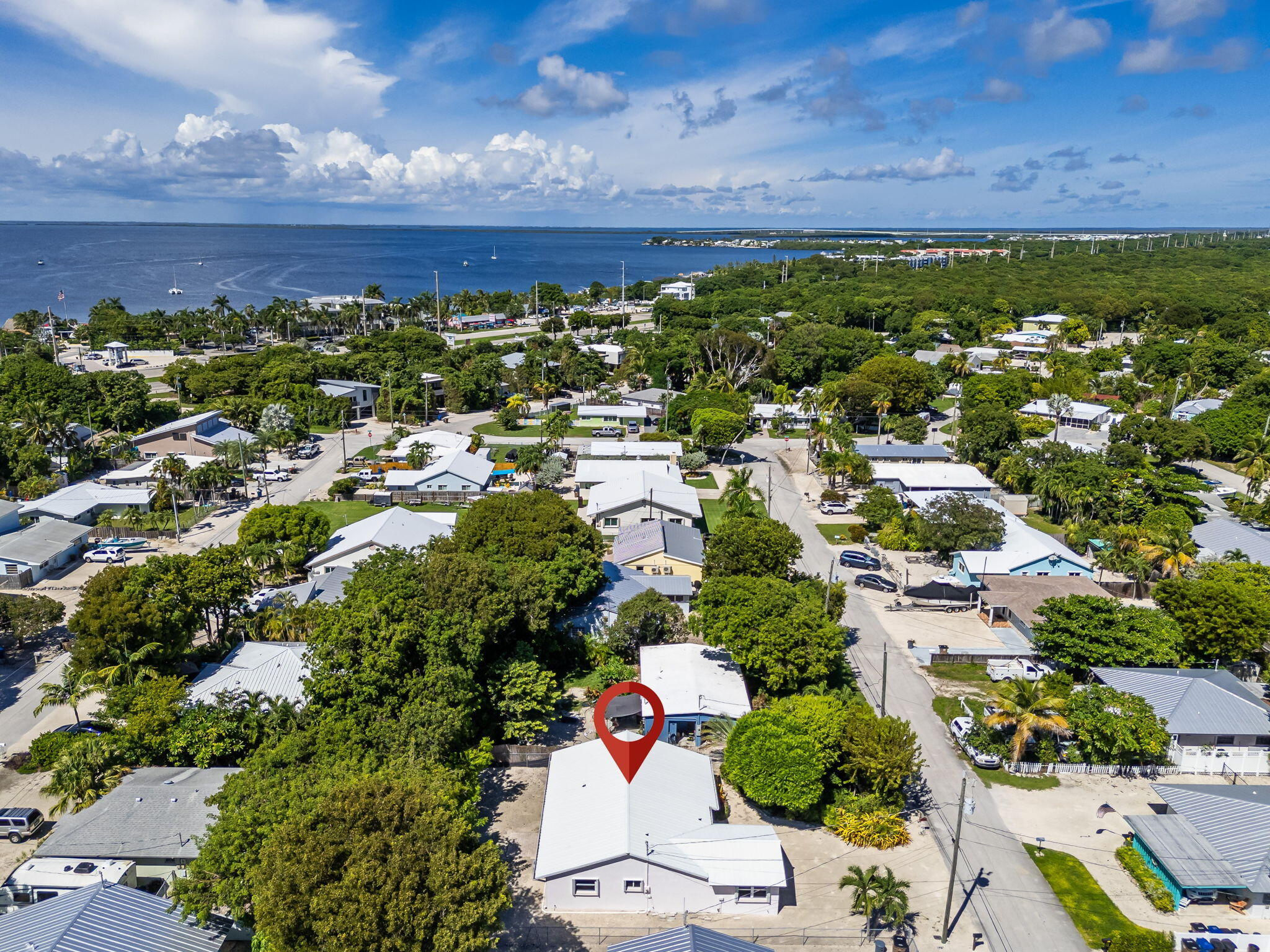 Aerial view of a white-roofed home marked by a red pin, surrounded by trees near the water.