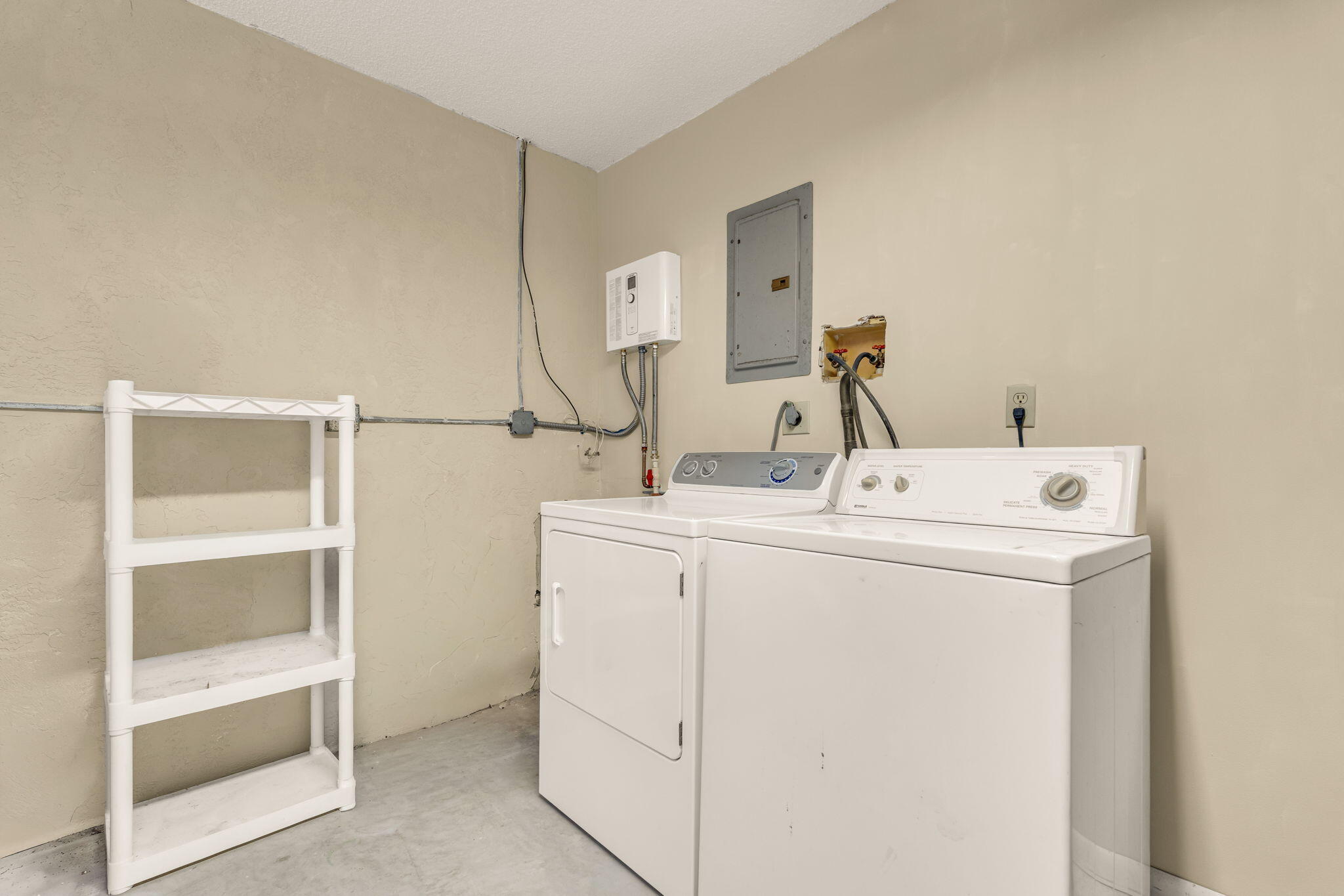Laundry room with a white washer and dryer beside an empty shelving unit.