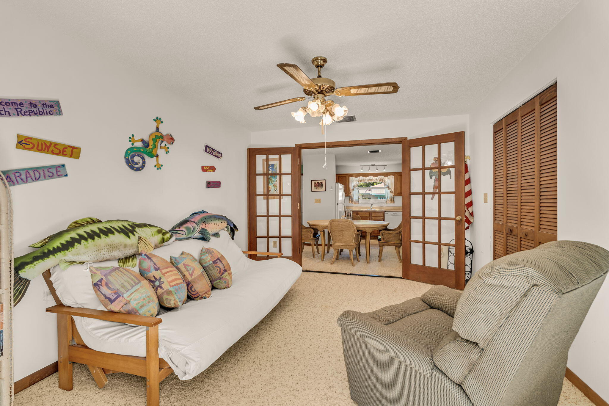 Furnished den with fish-themed pillows, tropical wall decorations, and open doors to the dining area.