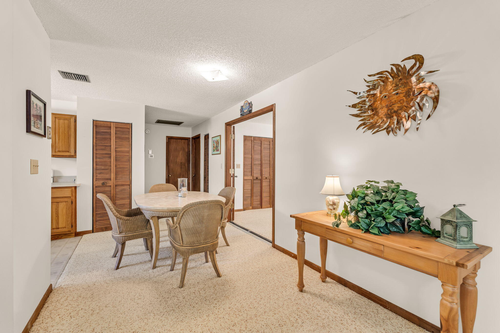 Dining area with wicker chairs, wooden louvered doors, and a metal sun wall sculpture.