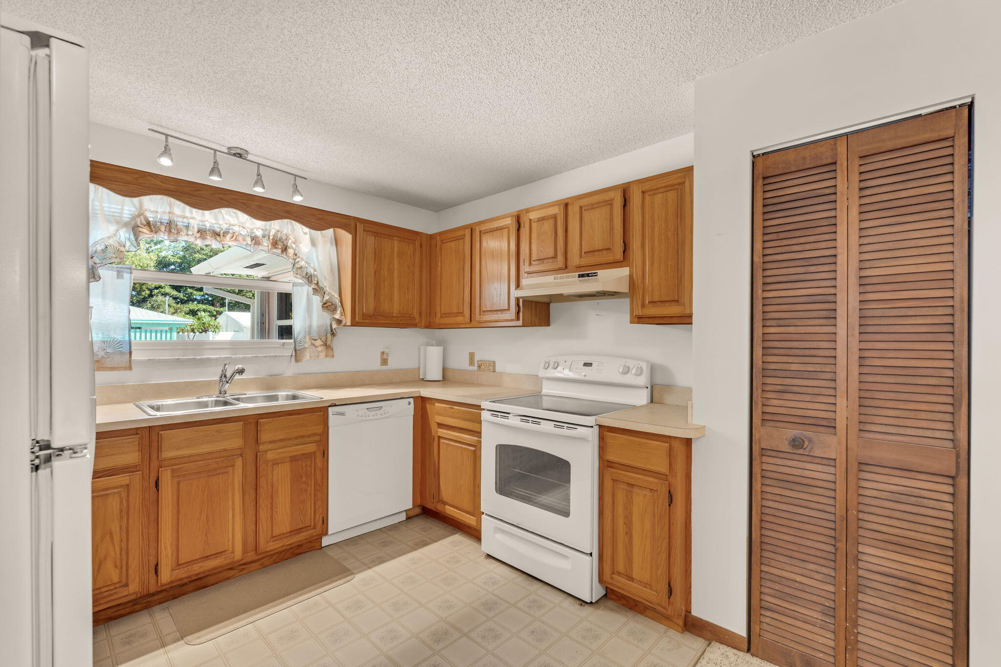 Kitchen with honey-colored cabinets, a double sink beneath a window, and white appliances.