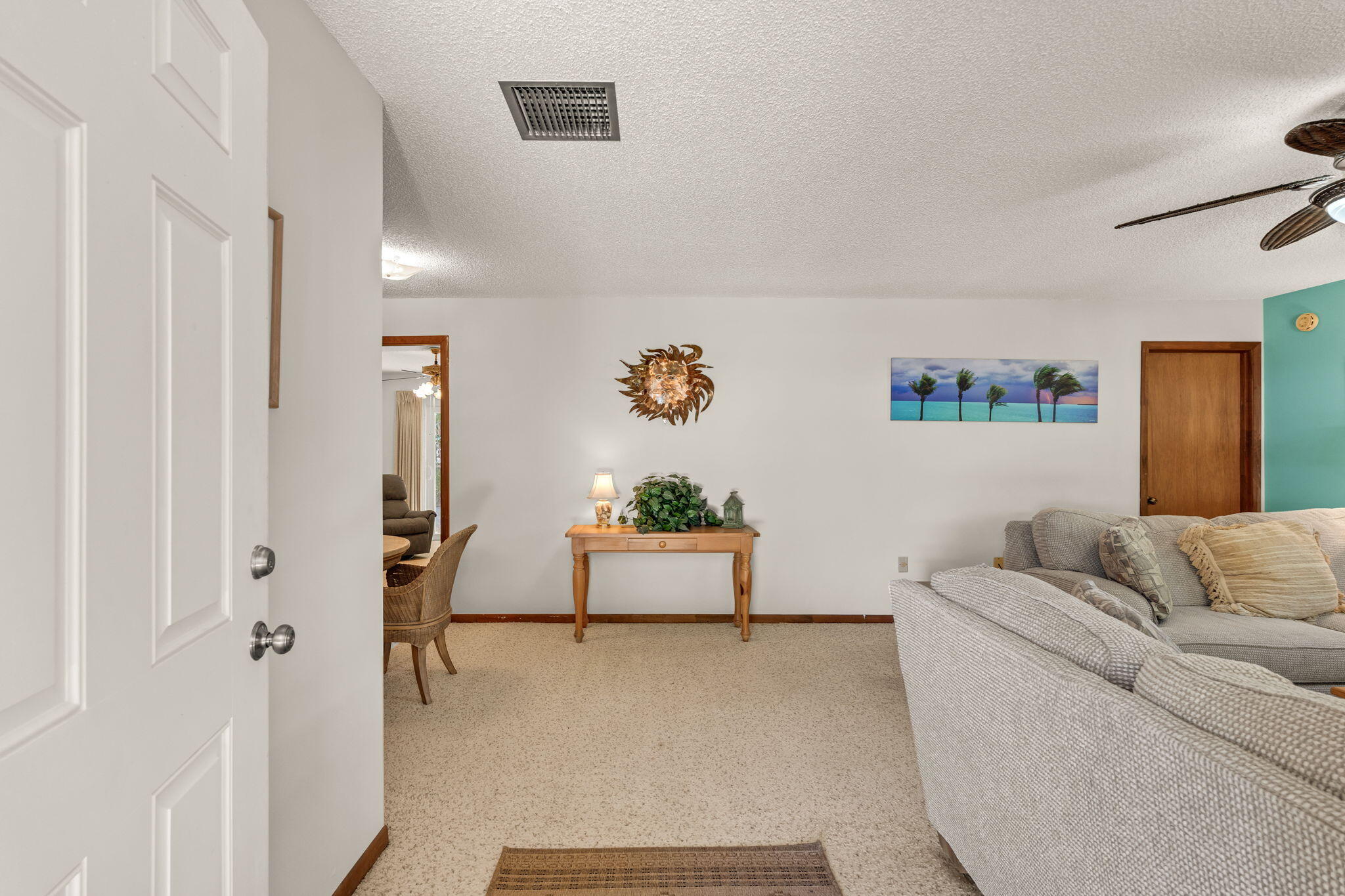 Living room with a gray sectional, carpeted floor, wooden console, and tropical wall art.