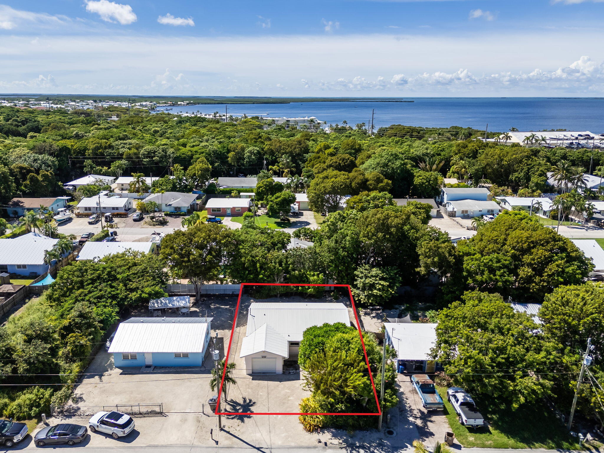 Aerial view of a home and red-outlined lot among leafy homes, with water in the distance.