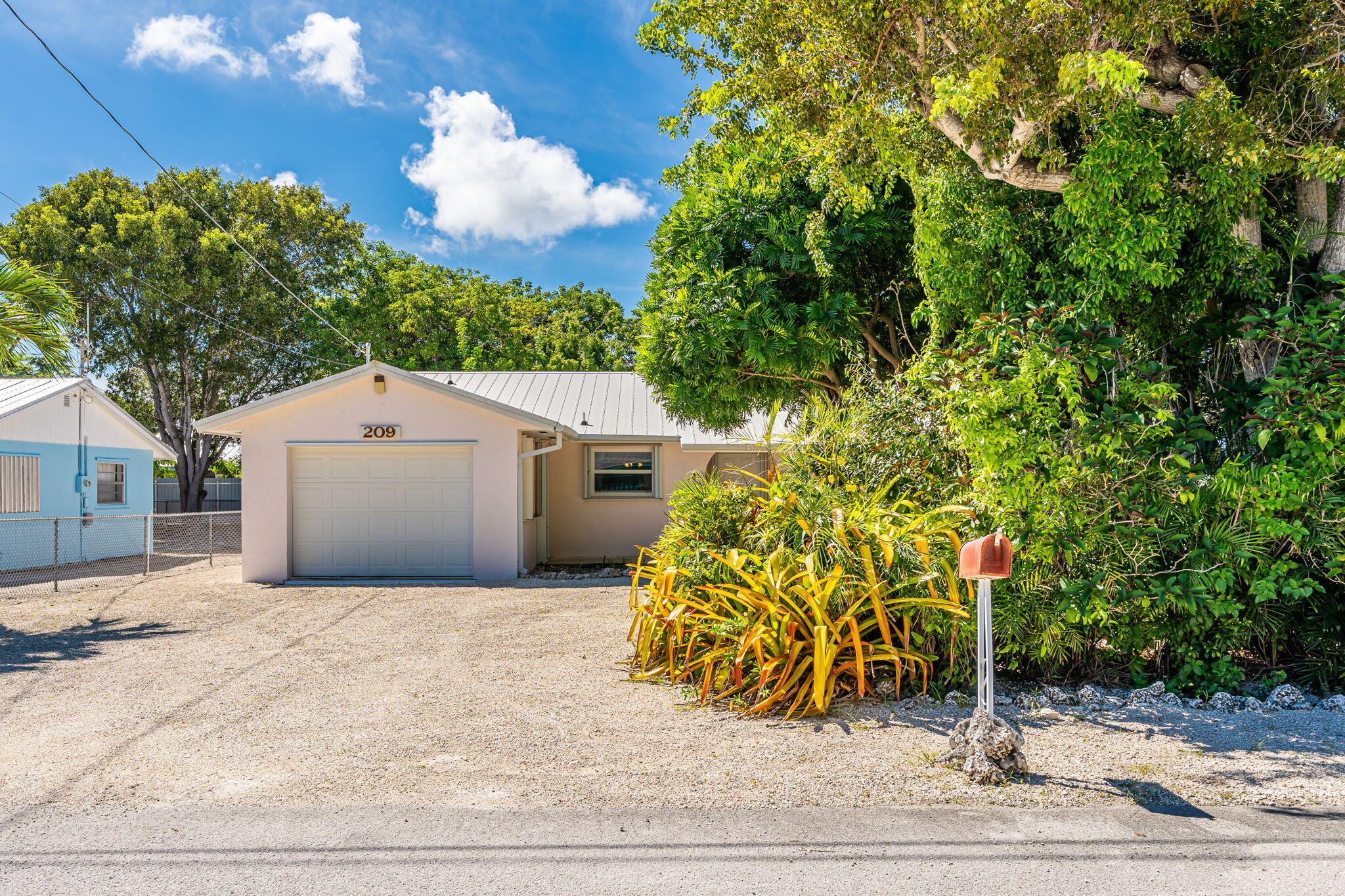 Home at 209 2nd Street with a front garage, gravel driveway, and tropical landscaping.