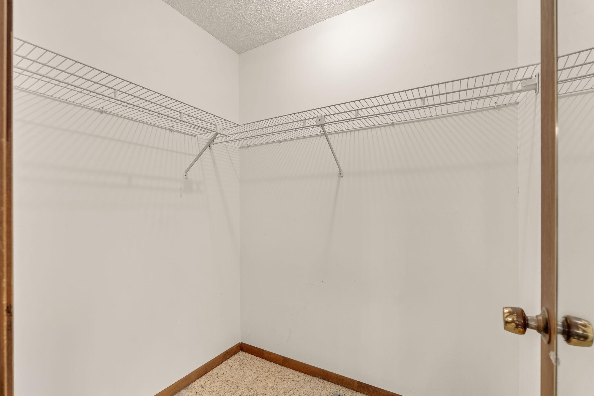 Empty walk-in closet with wraparound wire shelving and beige carpet.