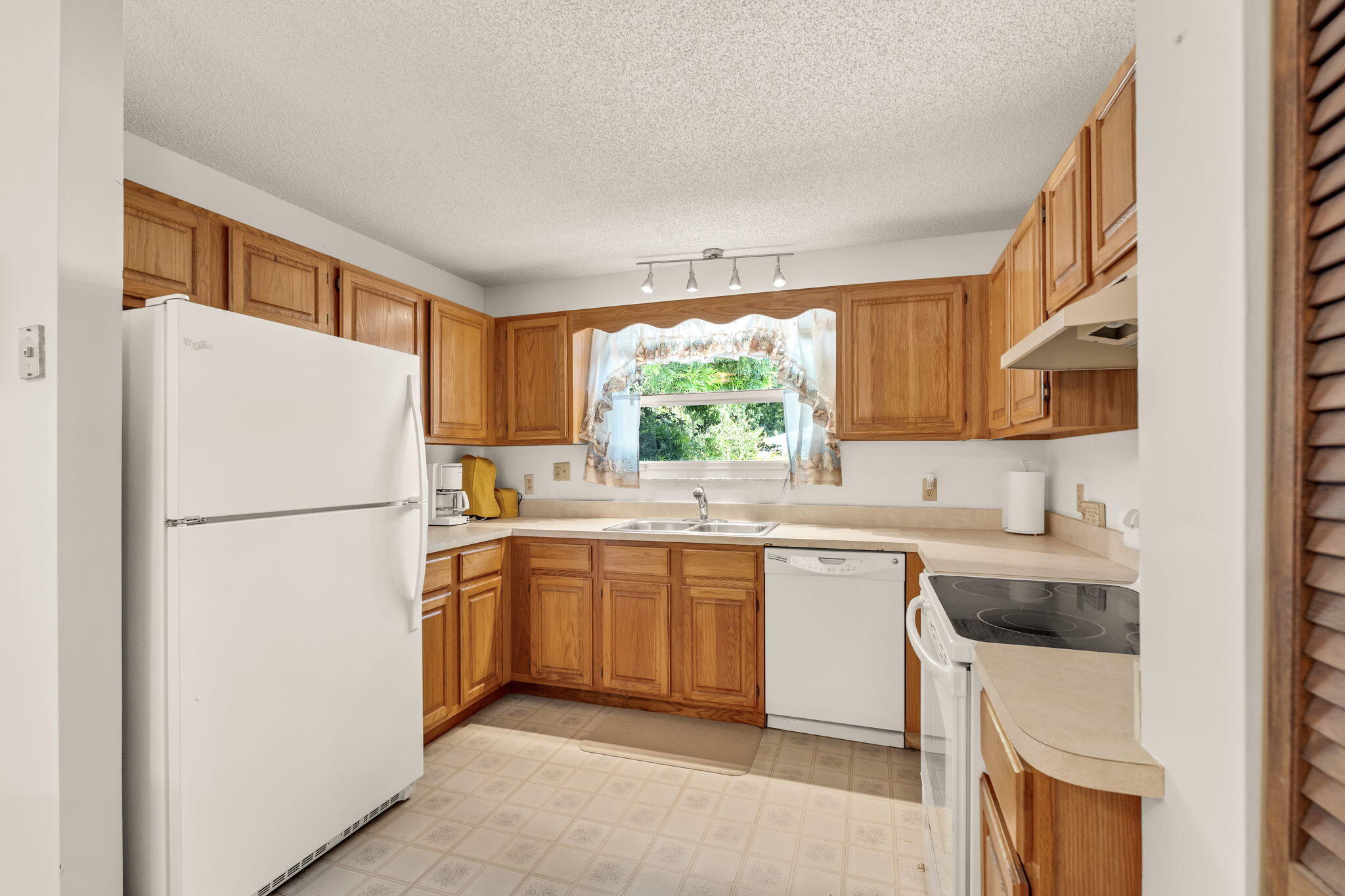Kitchen with honey-toned wood cabinets and a curtained window above the sink.