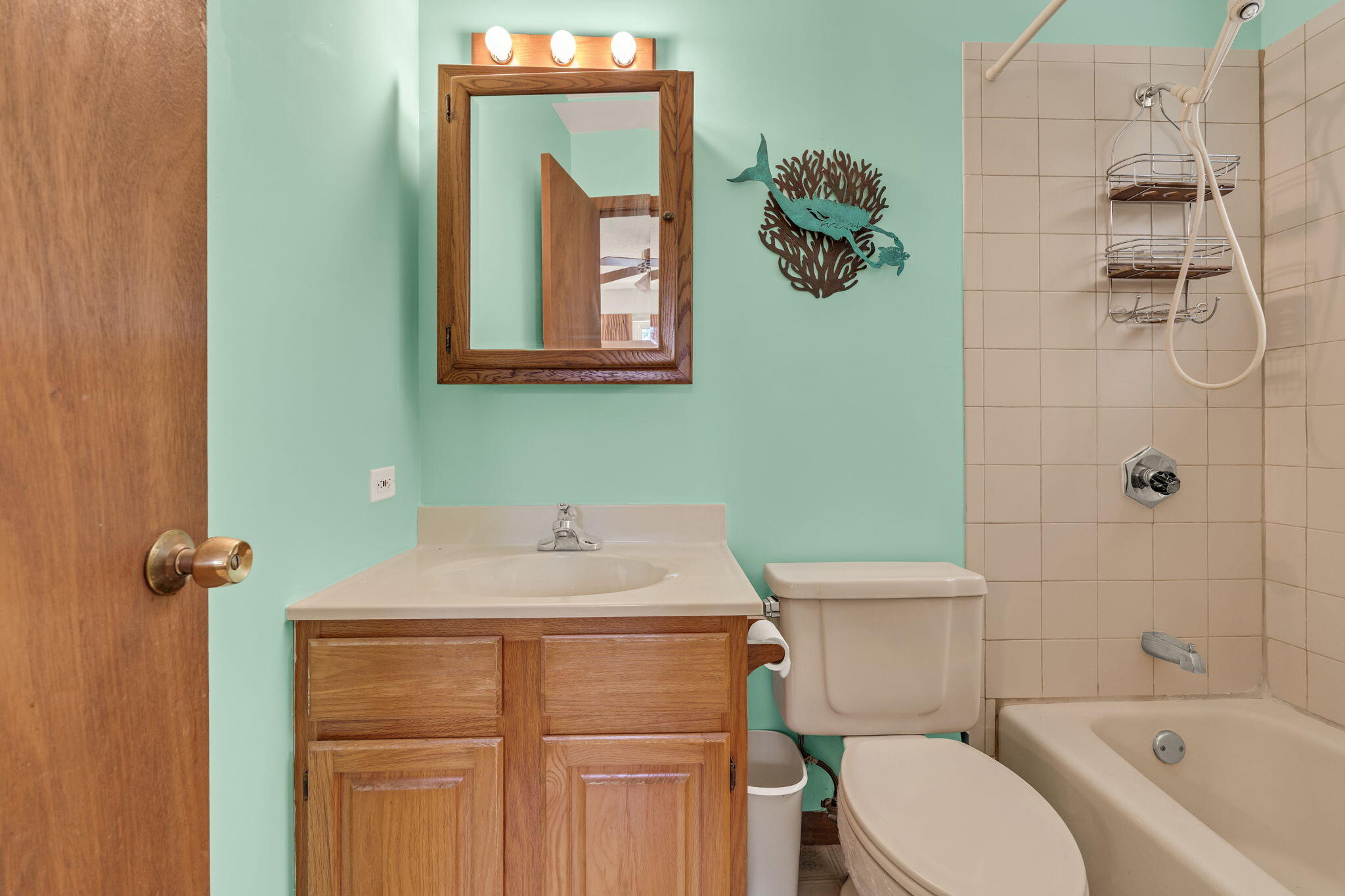 Bathroom with mint-green walls, wood vanity and mirror, and tiled tub-shower.