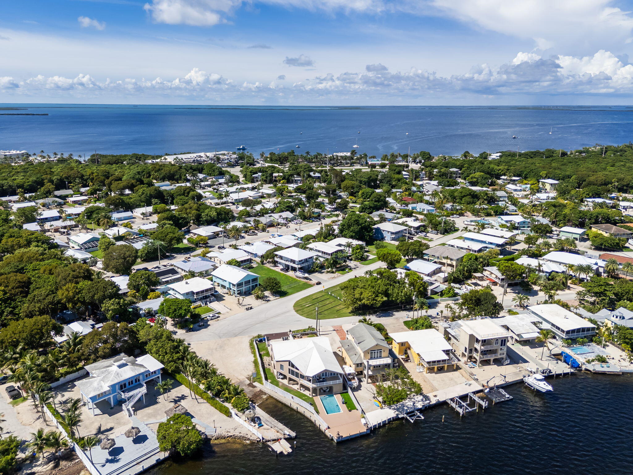 Aerial view of waterfront homes with docks and a pool beside open water.