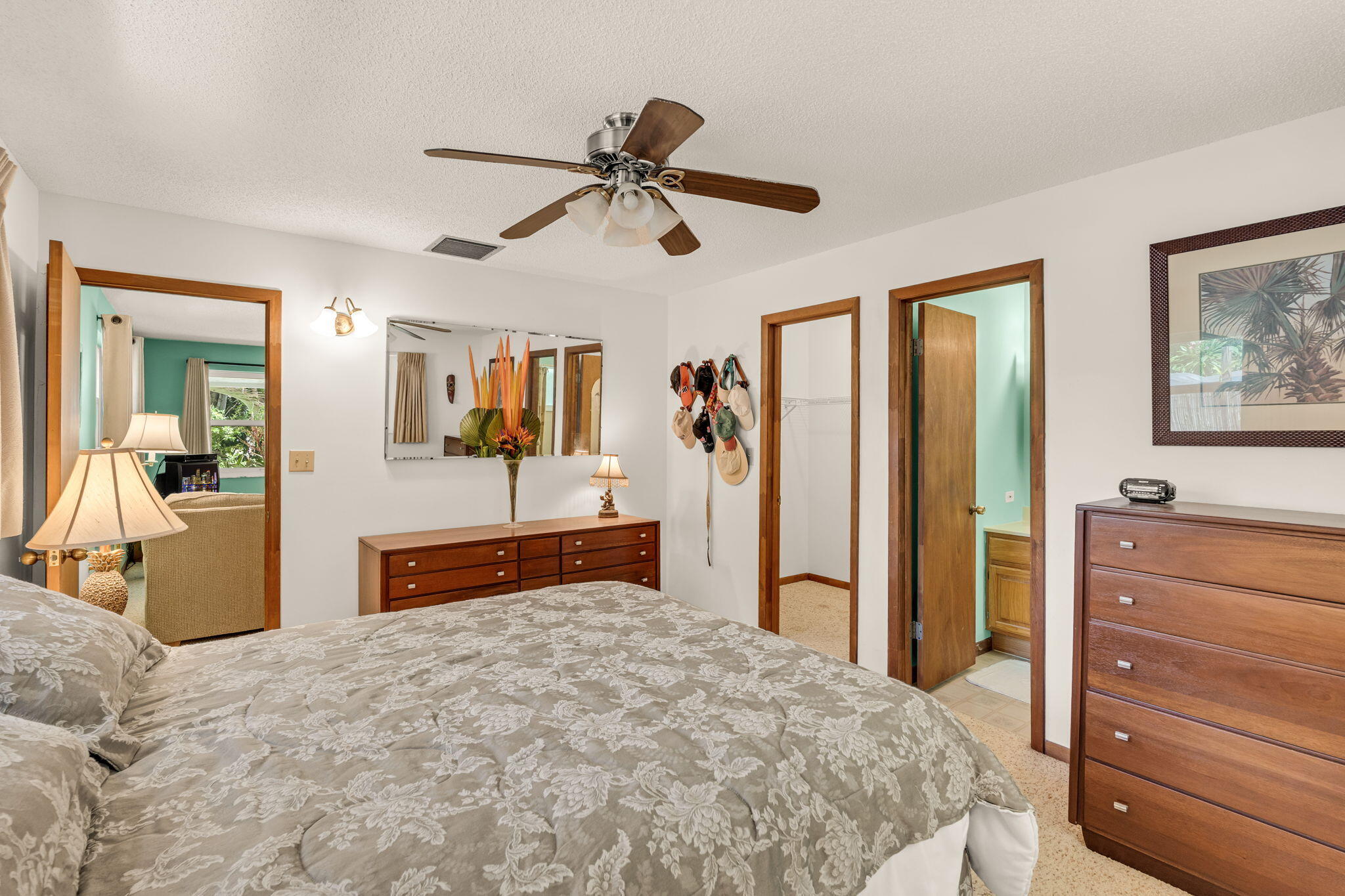 Furnished bedroom with a floral bedspread, wooden dressers, and a ceiling fan.