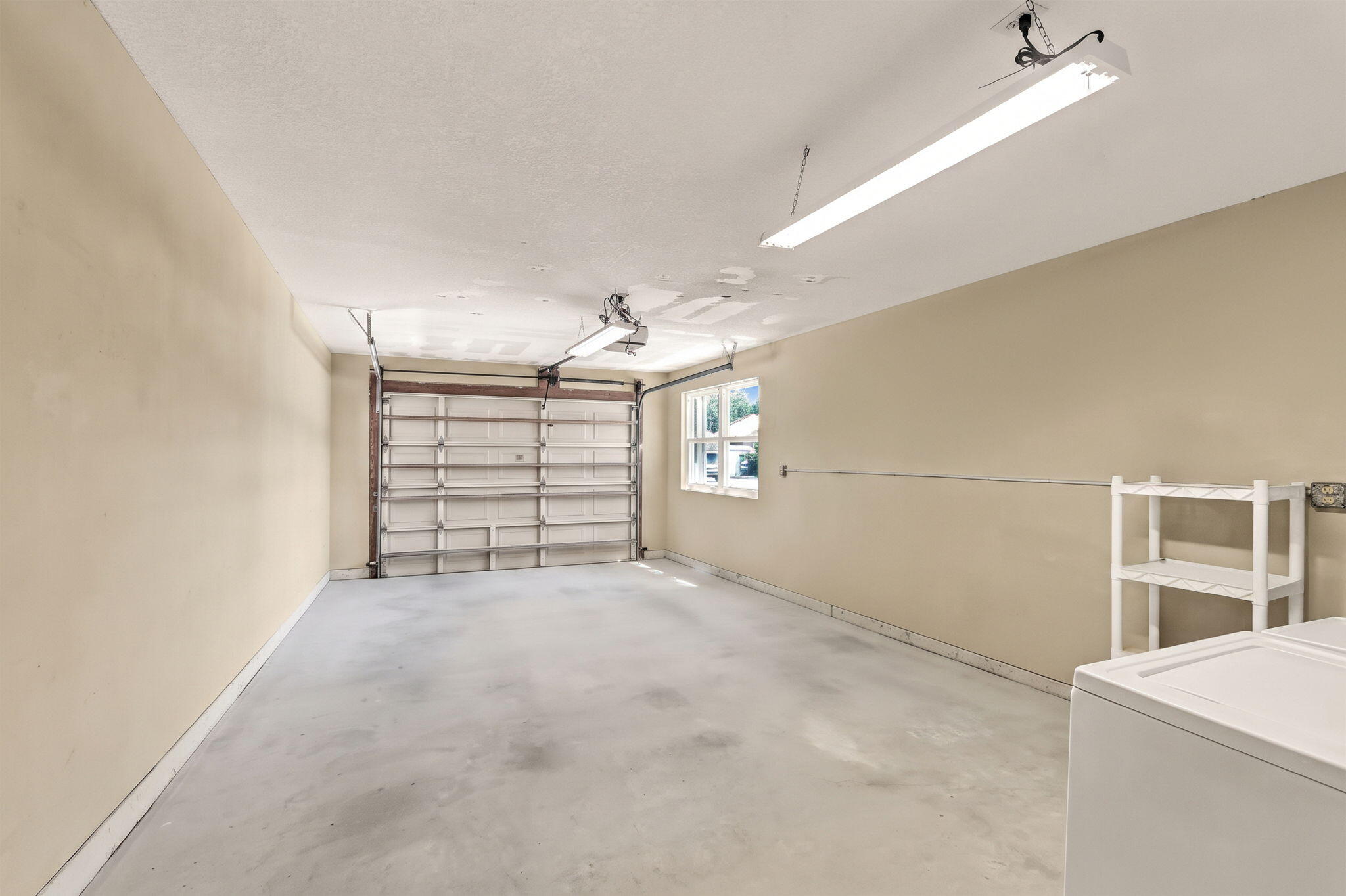 Vacant garage with a concrete floor, closed garage door, small window, and white shelving.