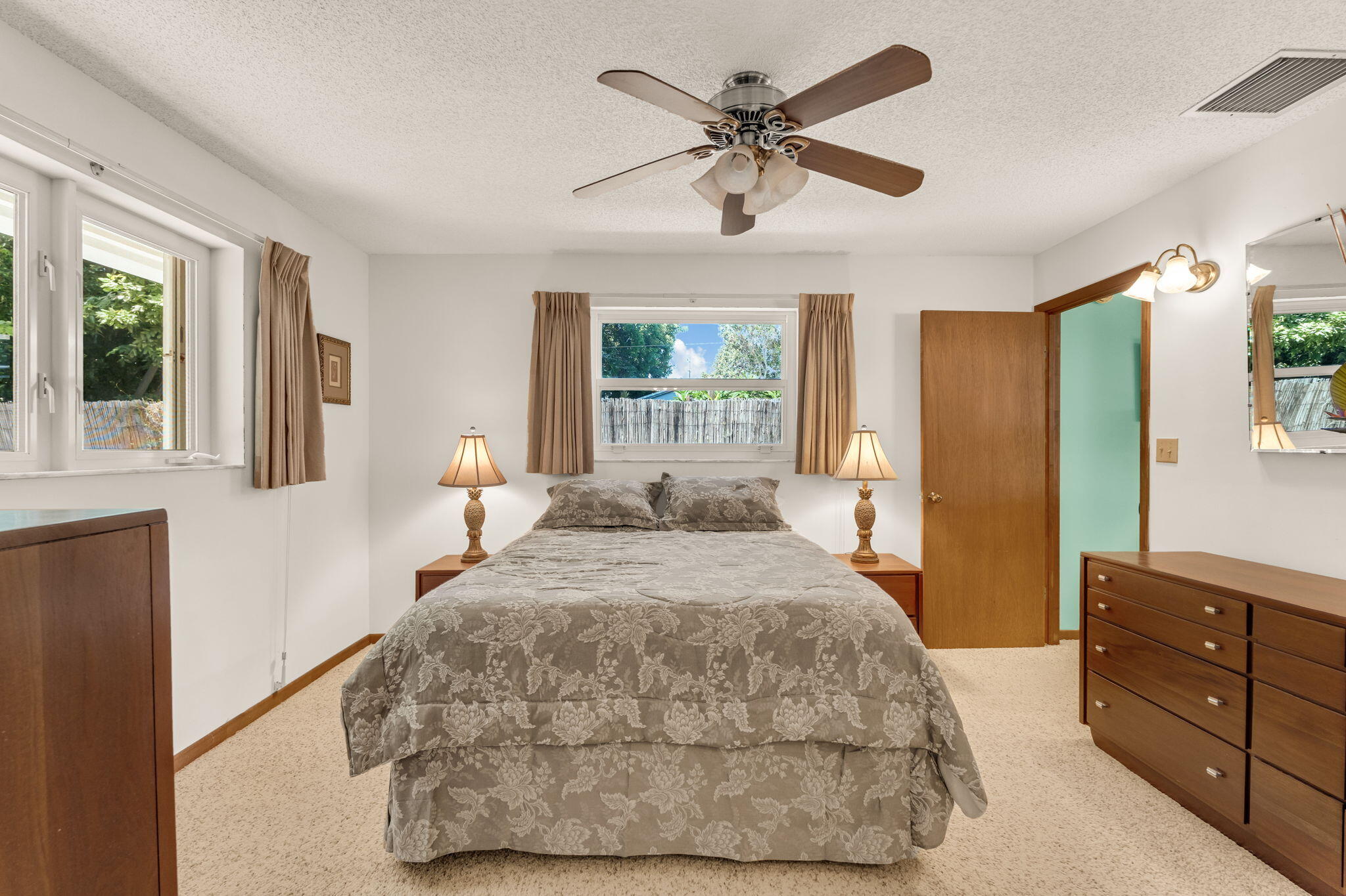Bedroom with a floral bed, matching lamps, curtained windows, and wooden dresser.