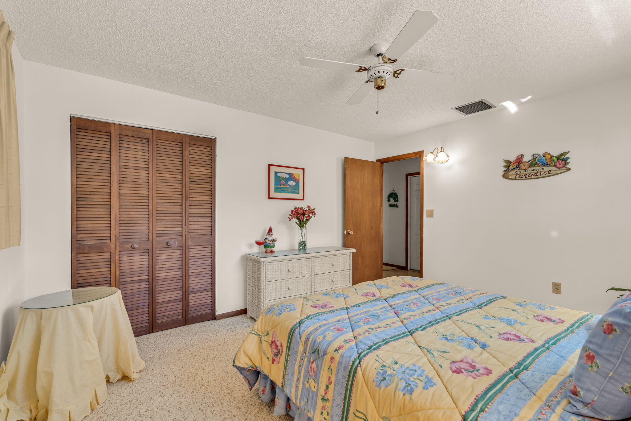 Bedroom with a colorful floral quilt, wooden louvered closet doors, and a white dresser.