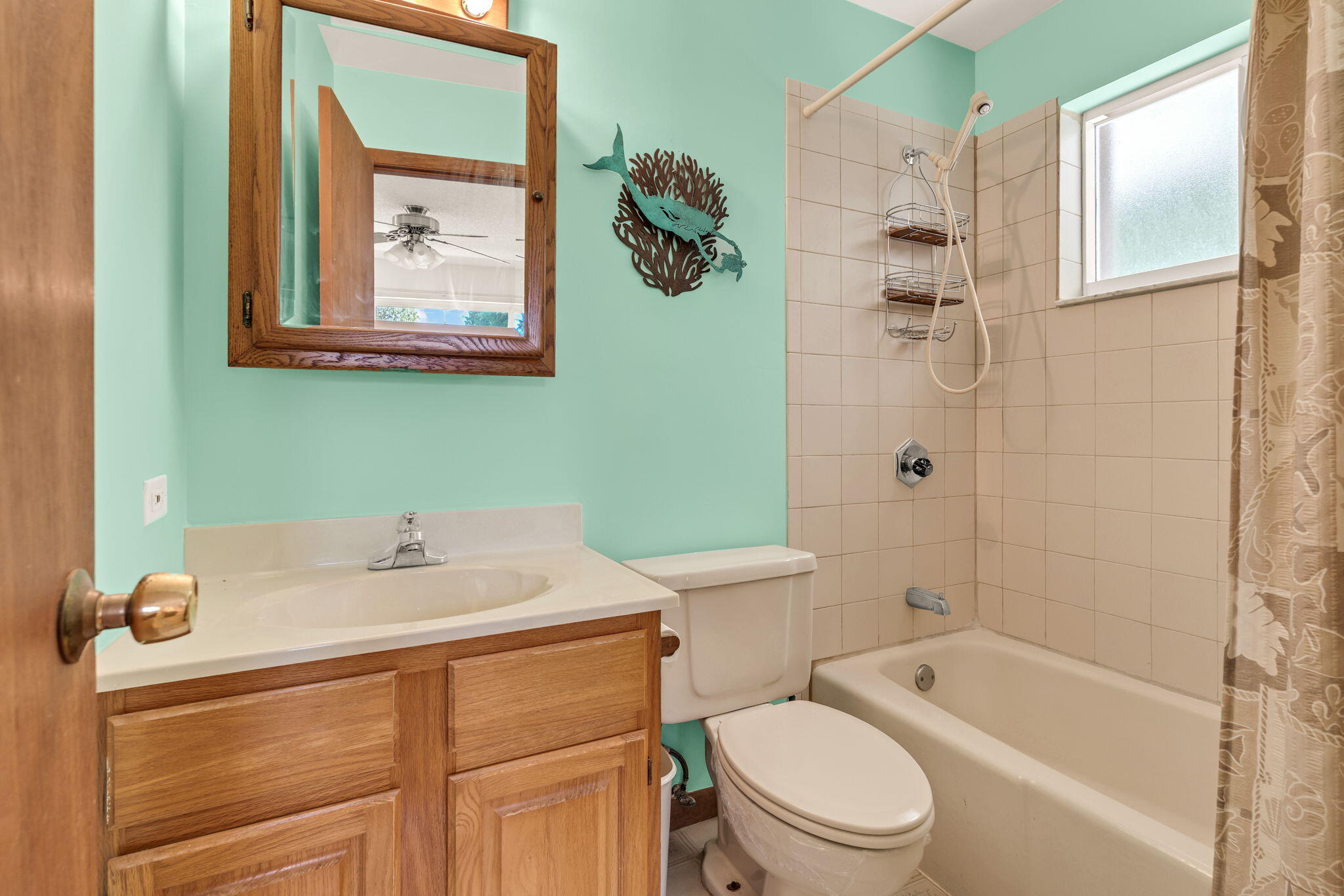 Bathroom with a wood vanity, mint green walls, and a beige tiled tub and shower.