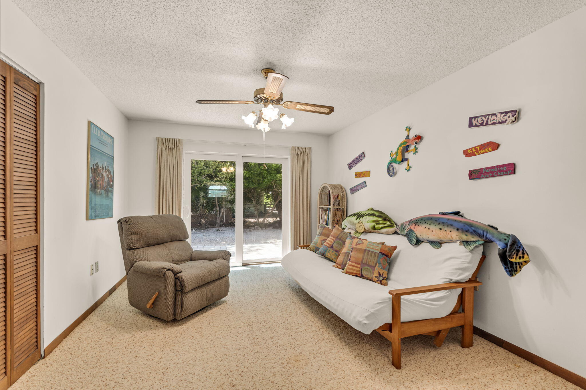 Furnished sitting room with recliner, fish-decorated sofa, and sliding glass doors to a leafy yard.