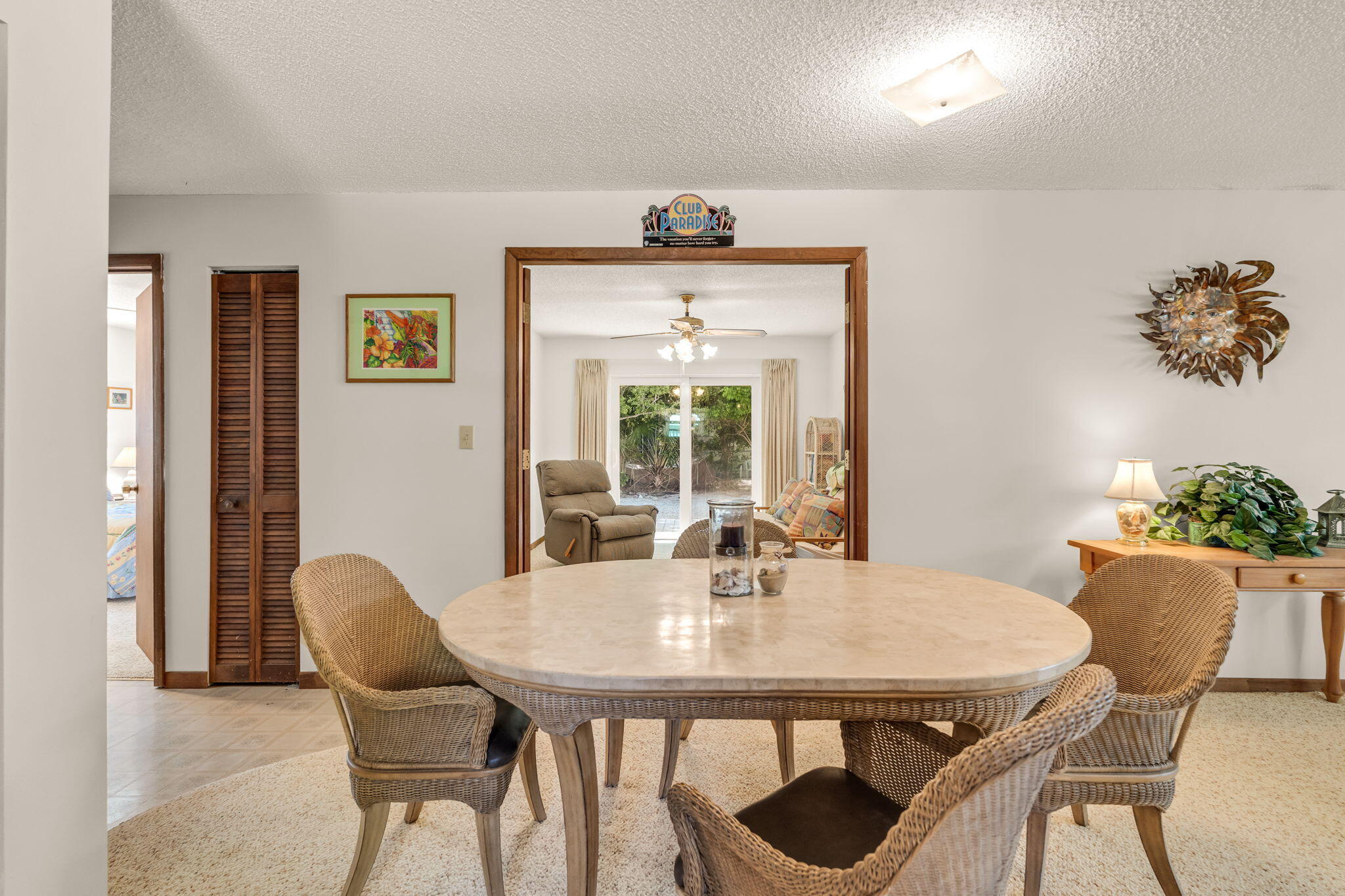Dining room with an oval table and wicker chairs, opening into a sitting room with sliding glass doors.