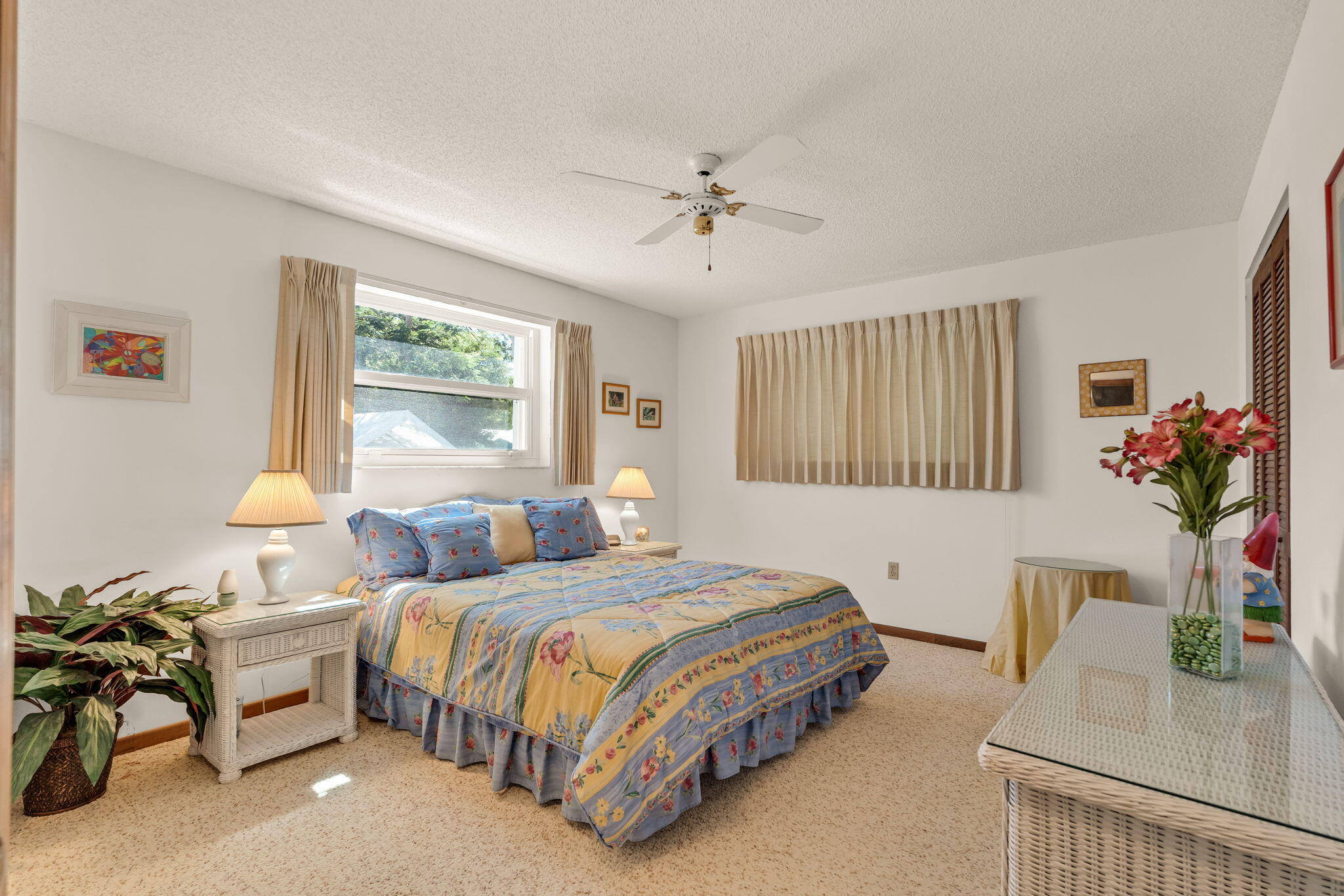 Bedroom with a floral quilted bed, beige curtains, and white wicker furniture.
